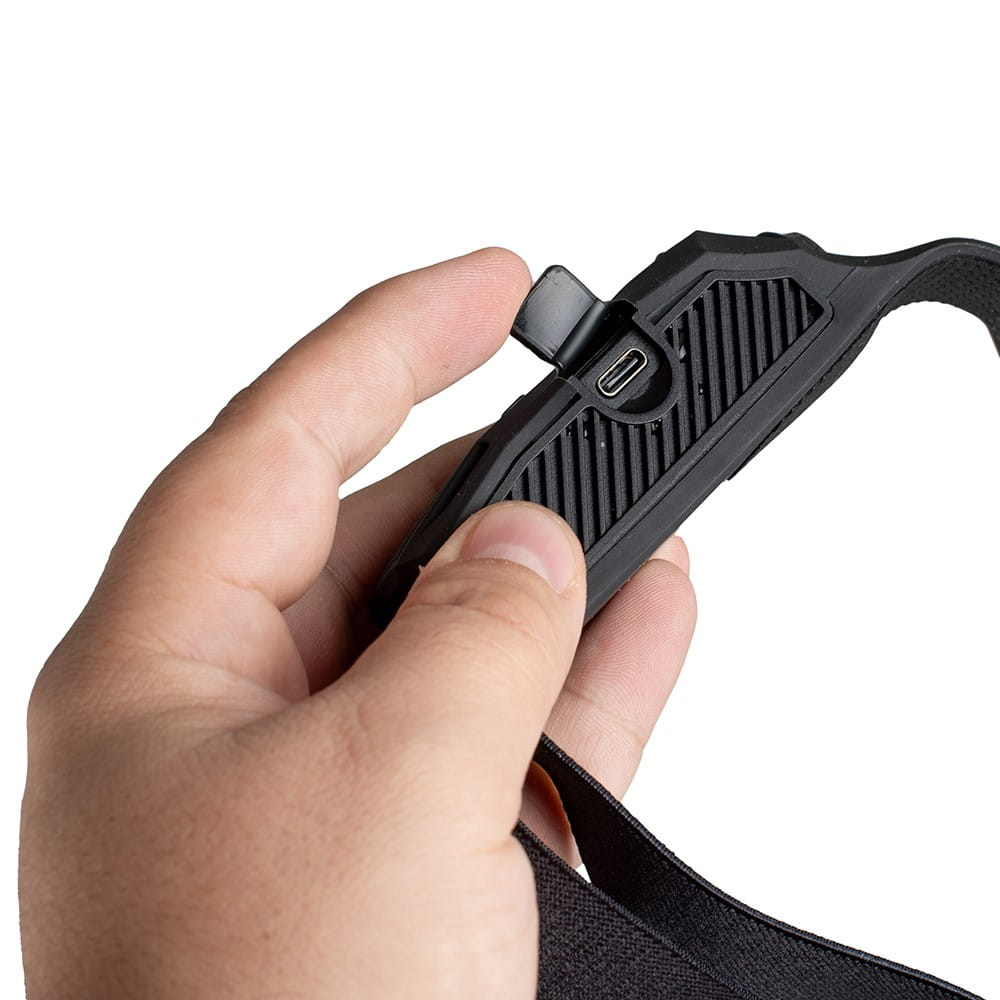 Dłoń trzymająca czarną latarkę czołową, pokazująca port USB.