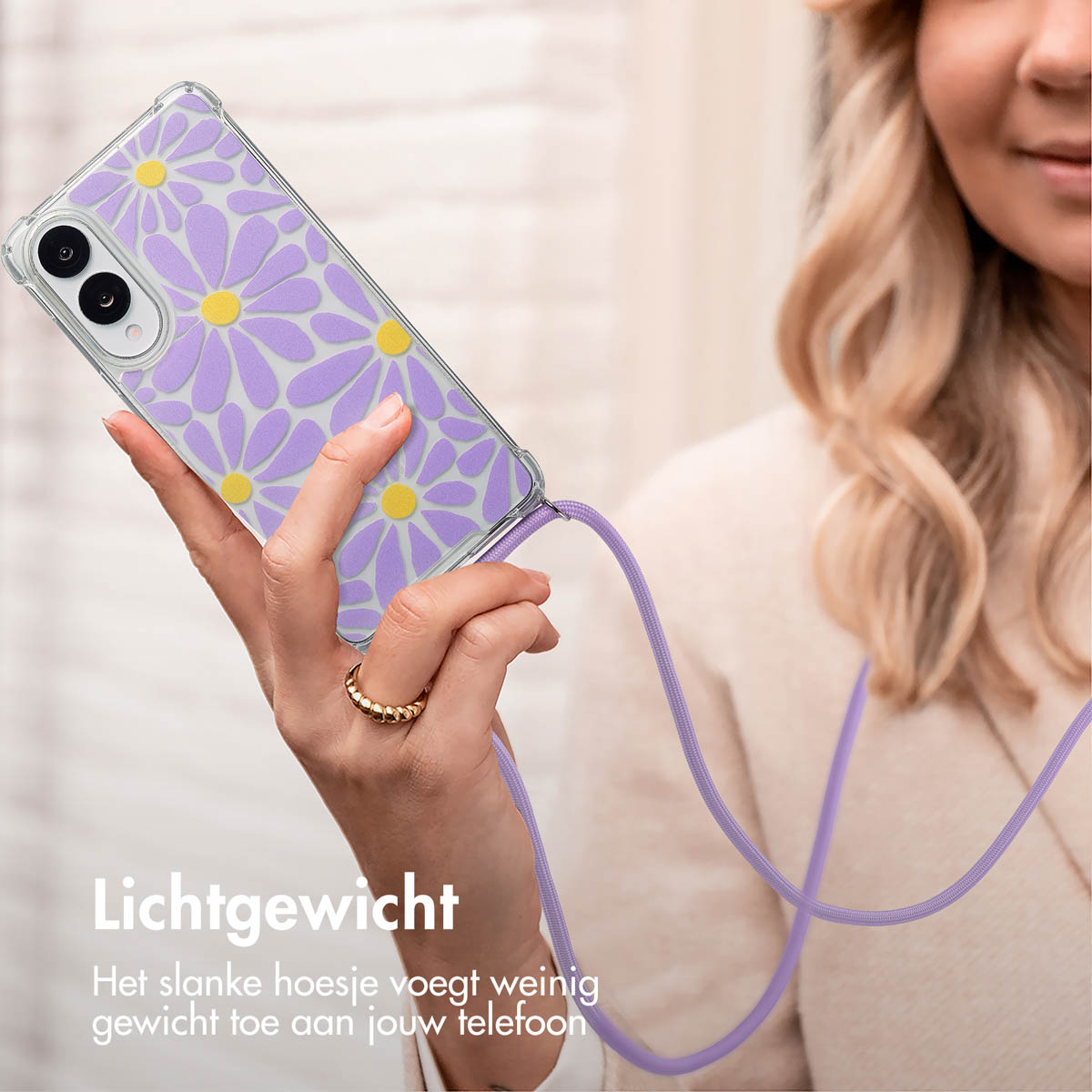 Transparante telefoonhoes met madeliefjesprint en paarse band. De hand van een vrouw houdt hem vast.