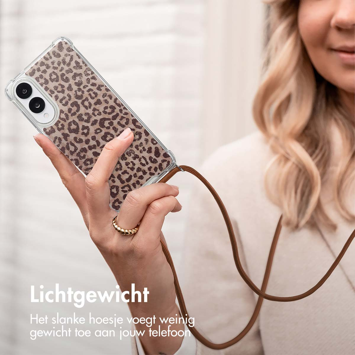 Een vrouw die een telefoon vasthoudt in een hoesje met luipaardprint en een bruin koord. De achtergrond is lichtbeige.