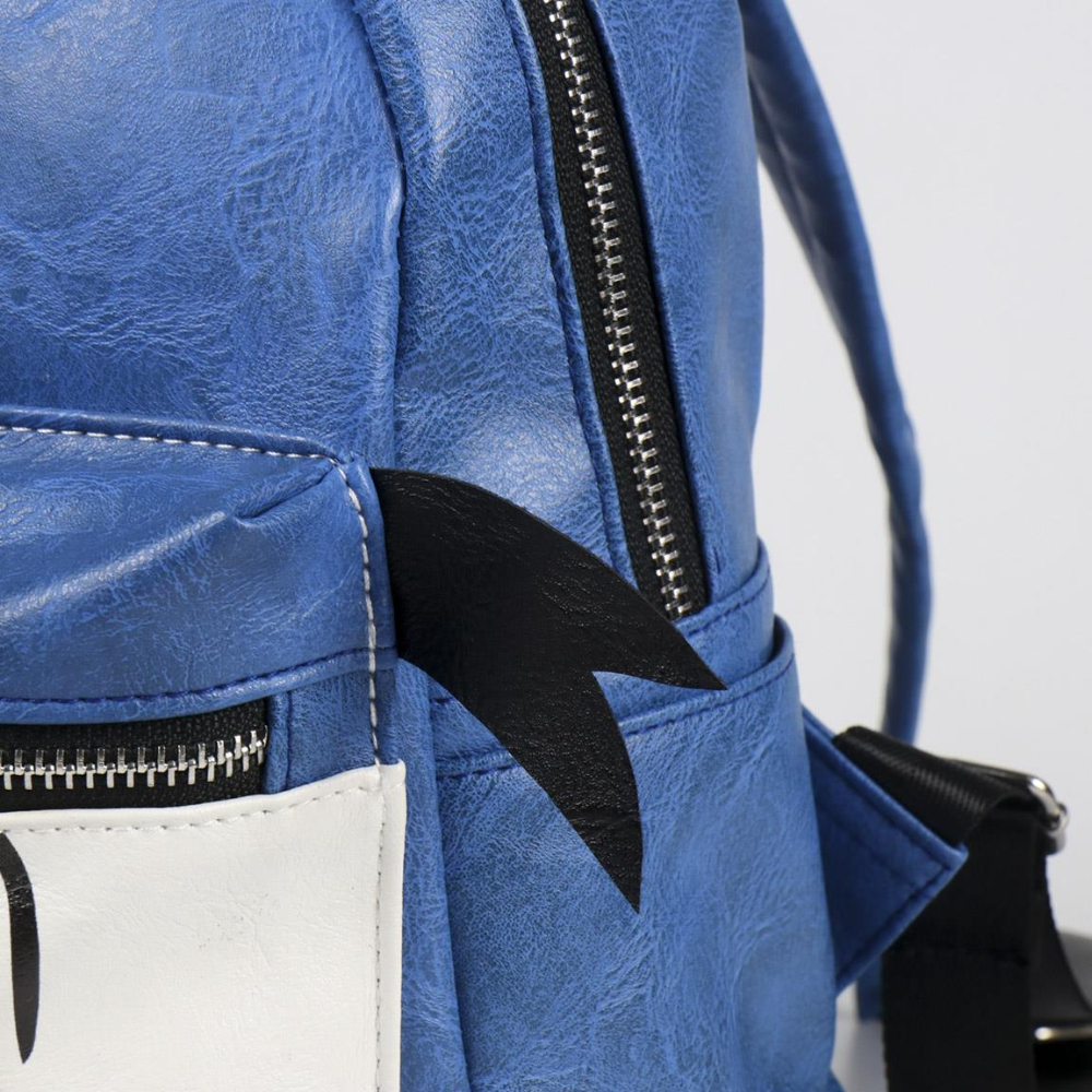 Primer plano de una mochila azul con una aleta negra. Cremallera negra y panel blanco con cara de dibujos animados.