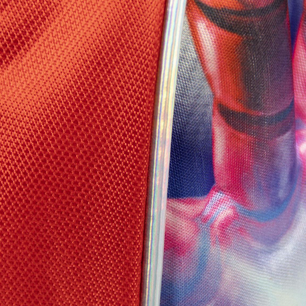 Primer plano de tela roja y una franja de metal plateado, con parte de una imagen visible.