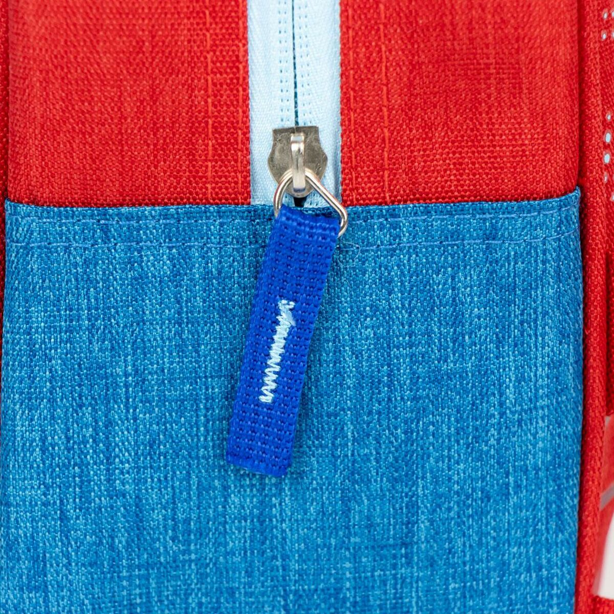 Primer plano de la cremallera de una mochila roja y azul con un tirador azul.