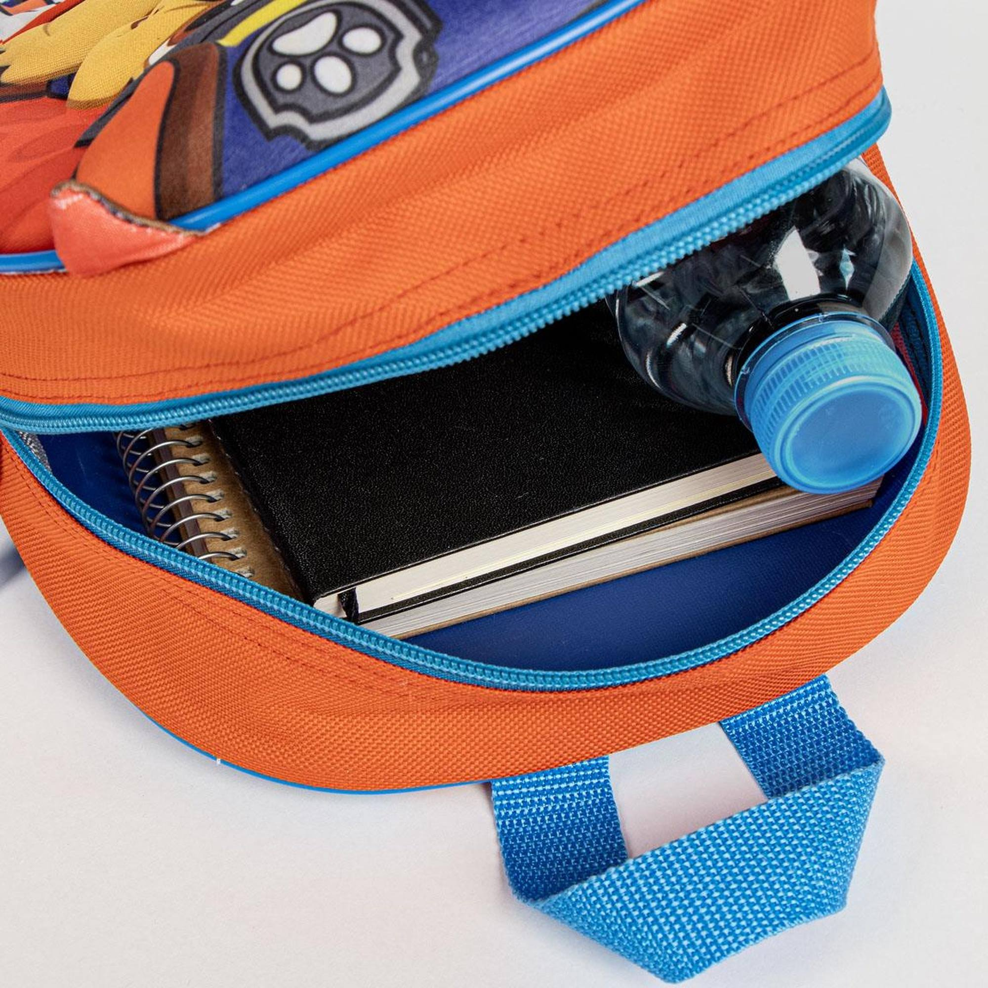 Detalle de mochila: exterior naranja con cremallera azul y cuaderno negro dentro.