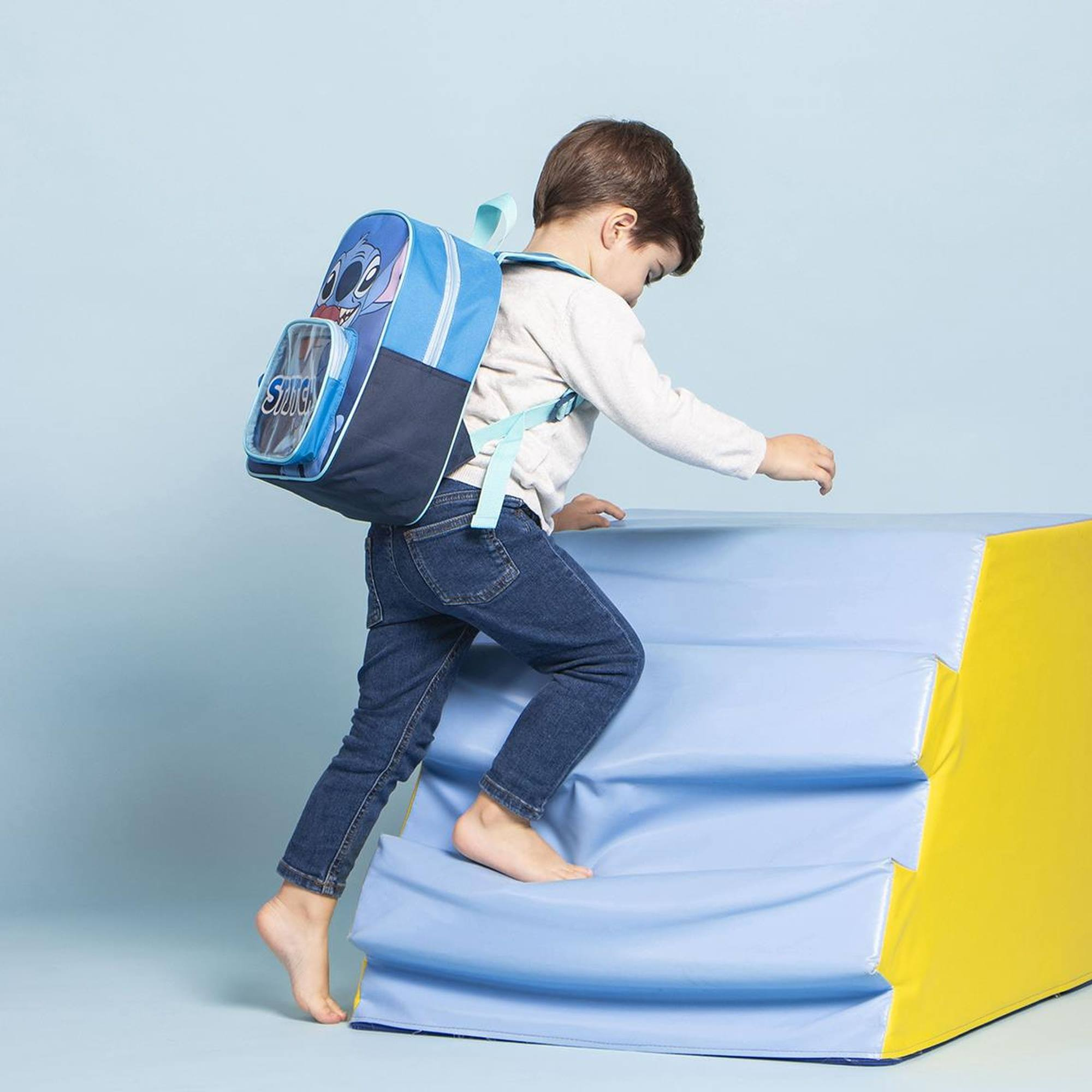 Un niño pequeño subiendo escalones azules con una mochila de Stitch. Fondo azul.