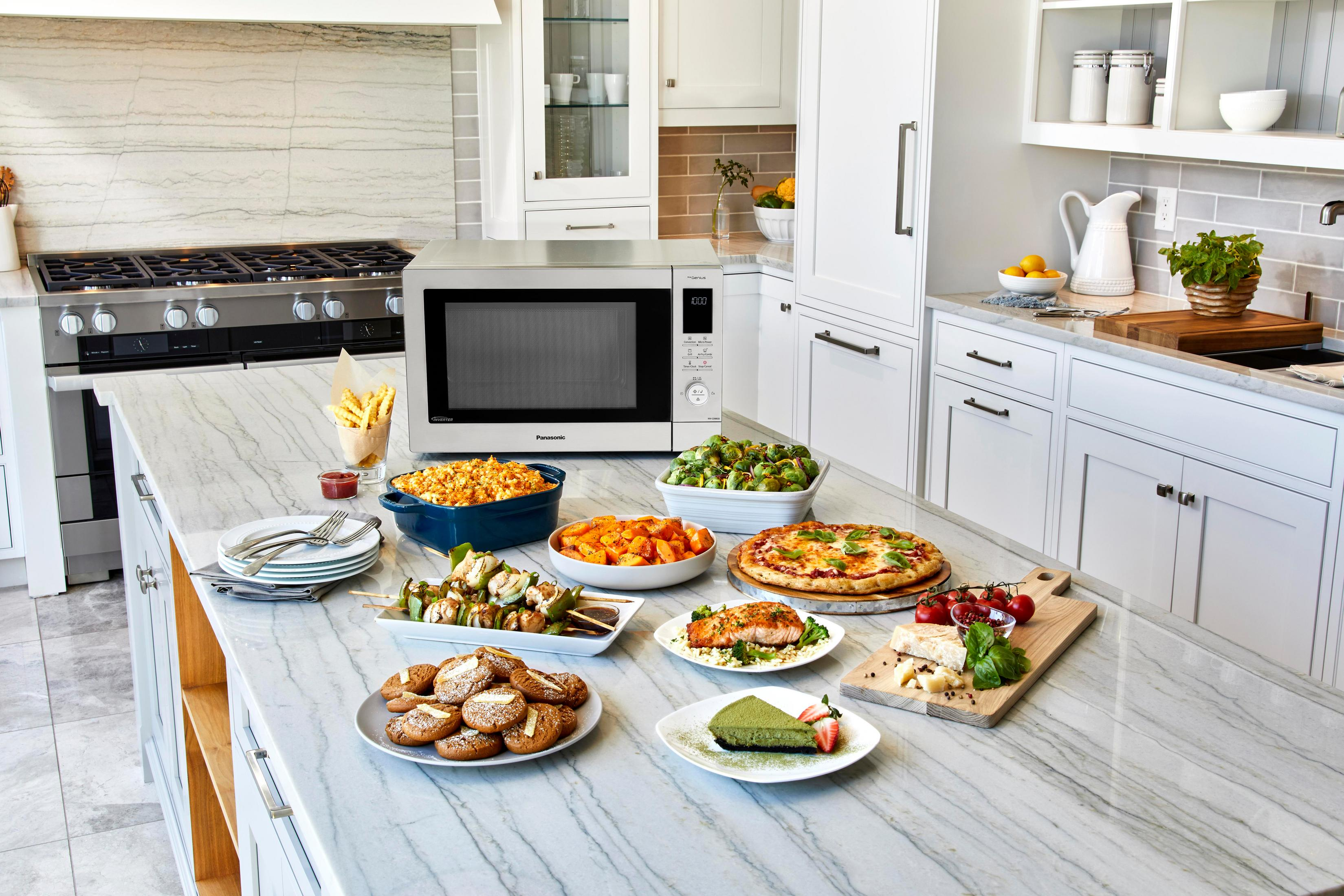 Blat kuchenny z wieloma daniami przygotowanego jedzenia i kuchenką mikrofalową Panasonic. Białe szafki w tle.