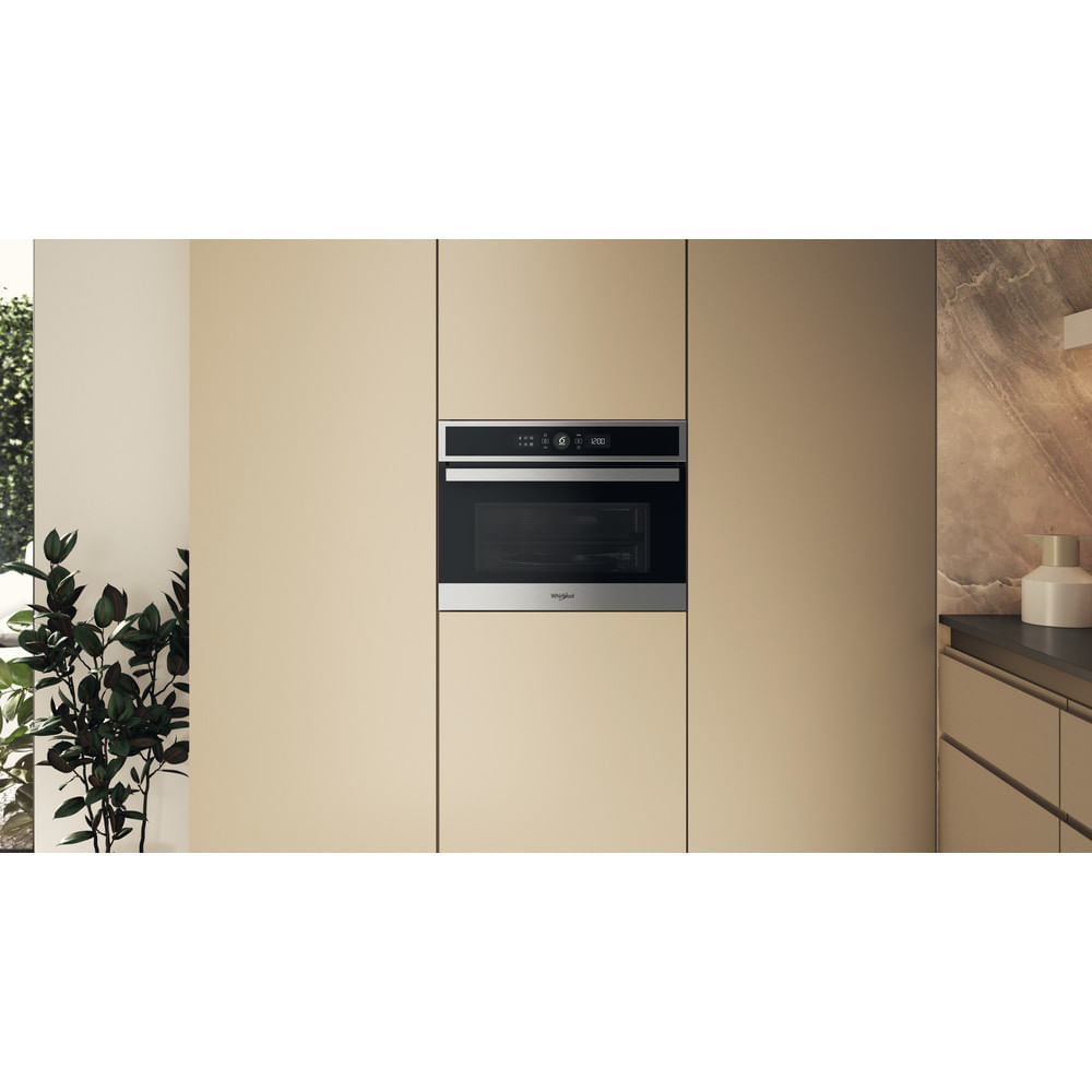 Cucina con mobili beige, forno a incasso e finestra. Una pianta vicino alla finestra.