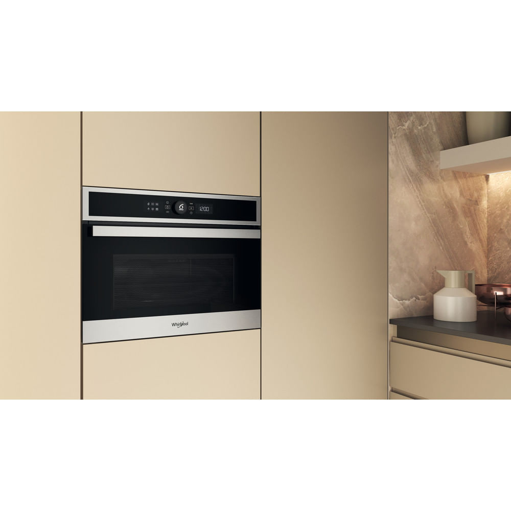 Forno a microonde Whirlpool integrato in una cucina. Il display digitale mostra 12:00. Mobile beige e parete marmorizzata.