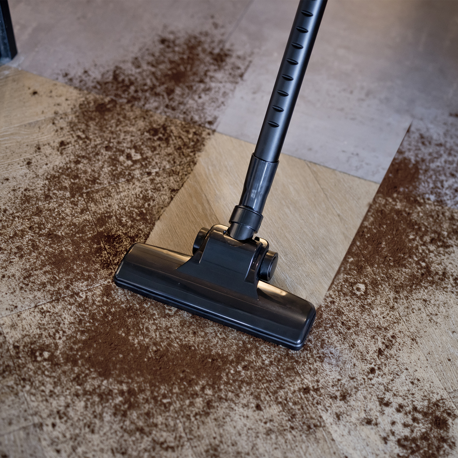 Vacuum cleaner cleaning a floor scattered with brown powder. Features a black head.