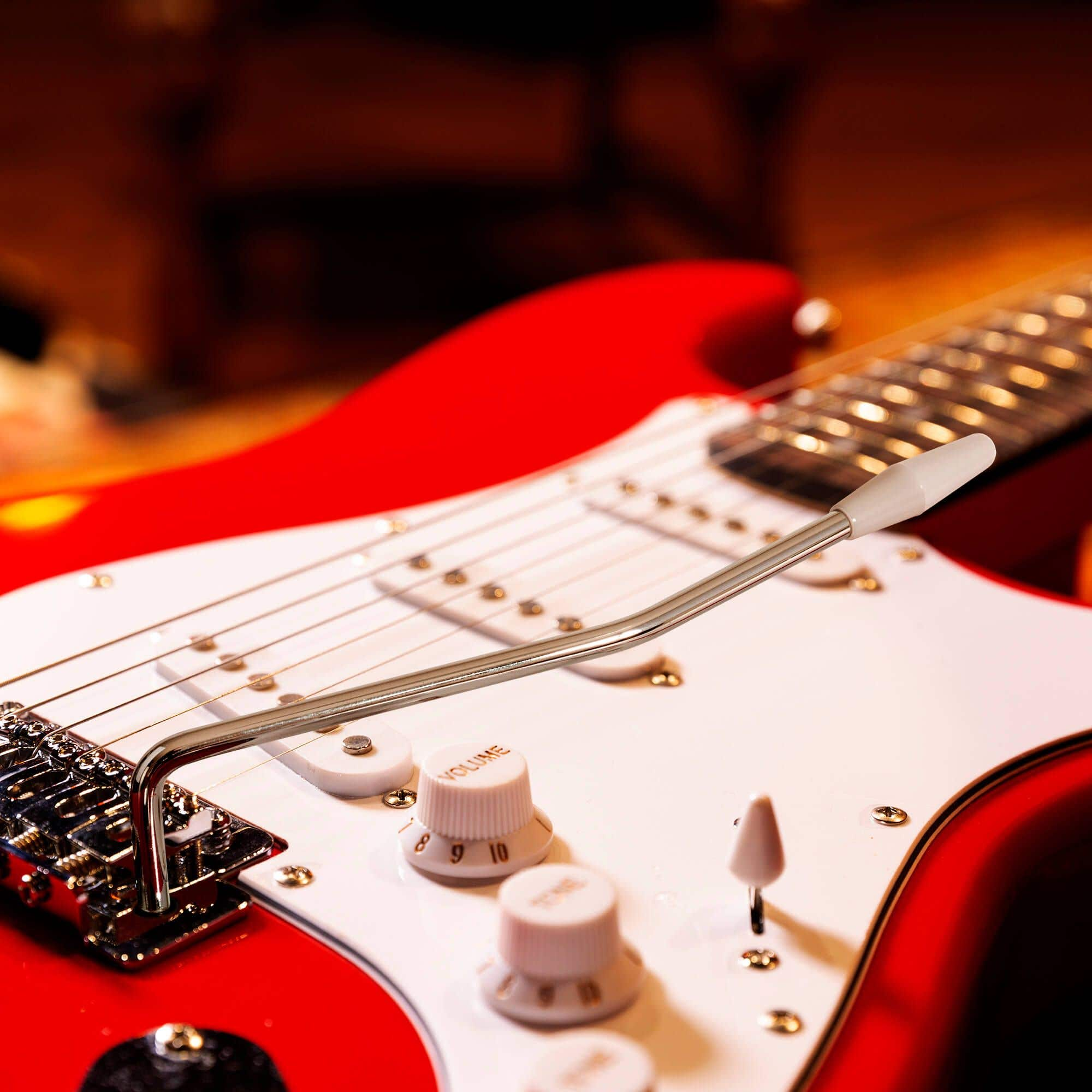 Gros plan sur le corps d'une guitare électrique rouge. Les boutons, les cordes et la barre de vibrato sont visibles.