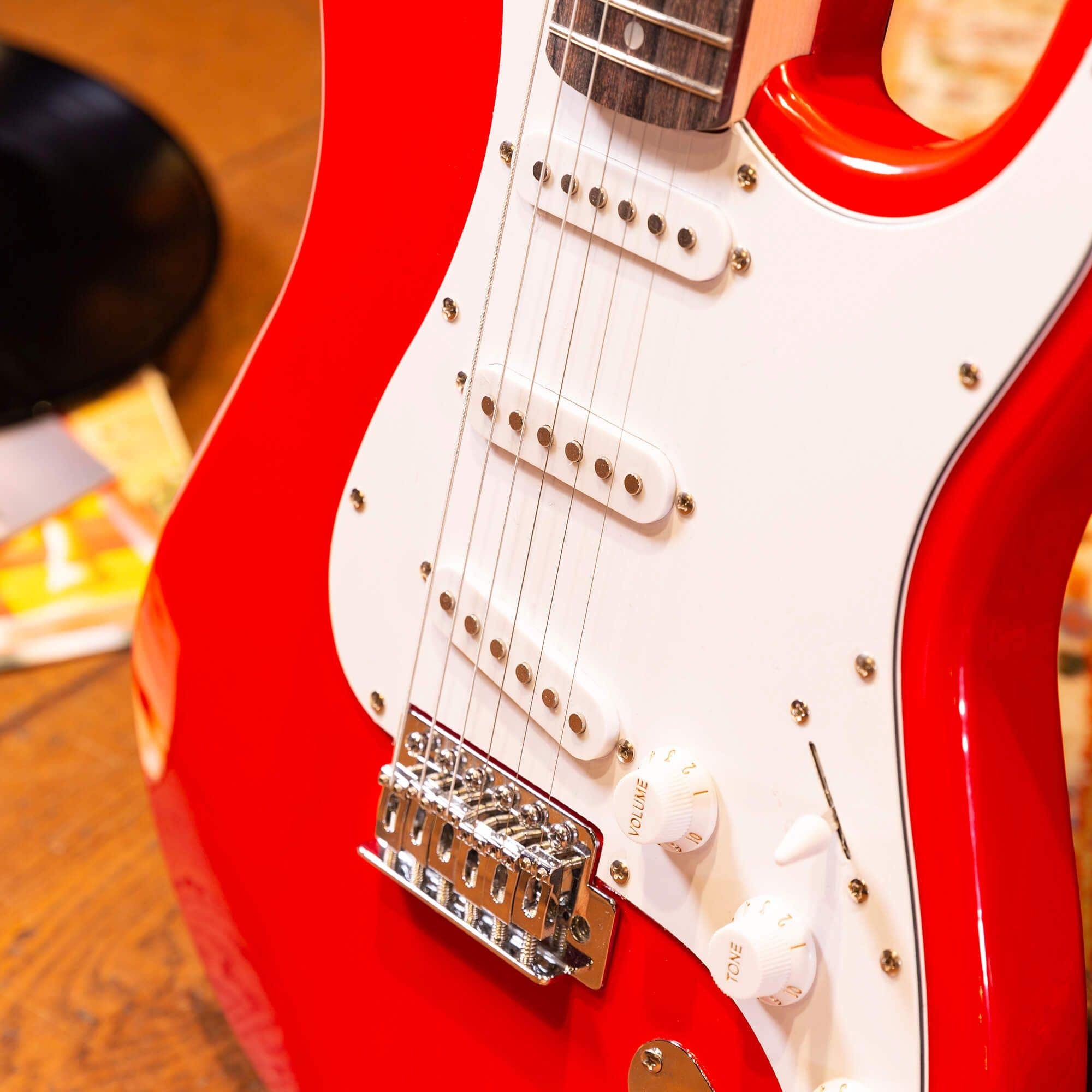 Gros plan sur une guitare électrique rouge montrant les cordes, les boutons de volume et de tonalité, et le chevalet.