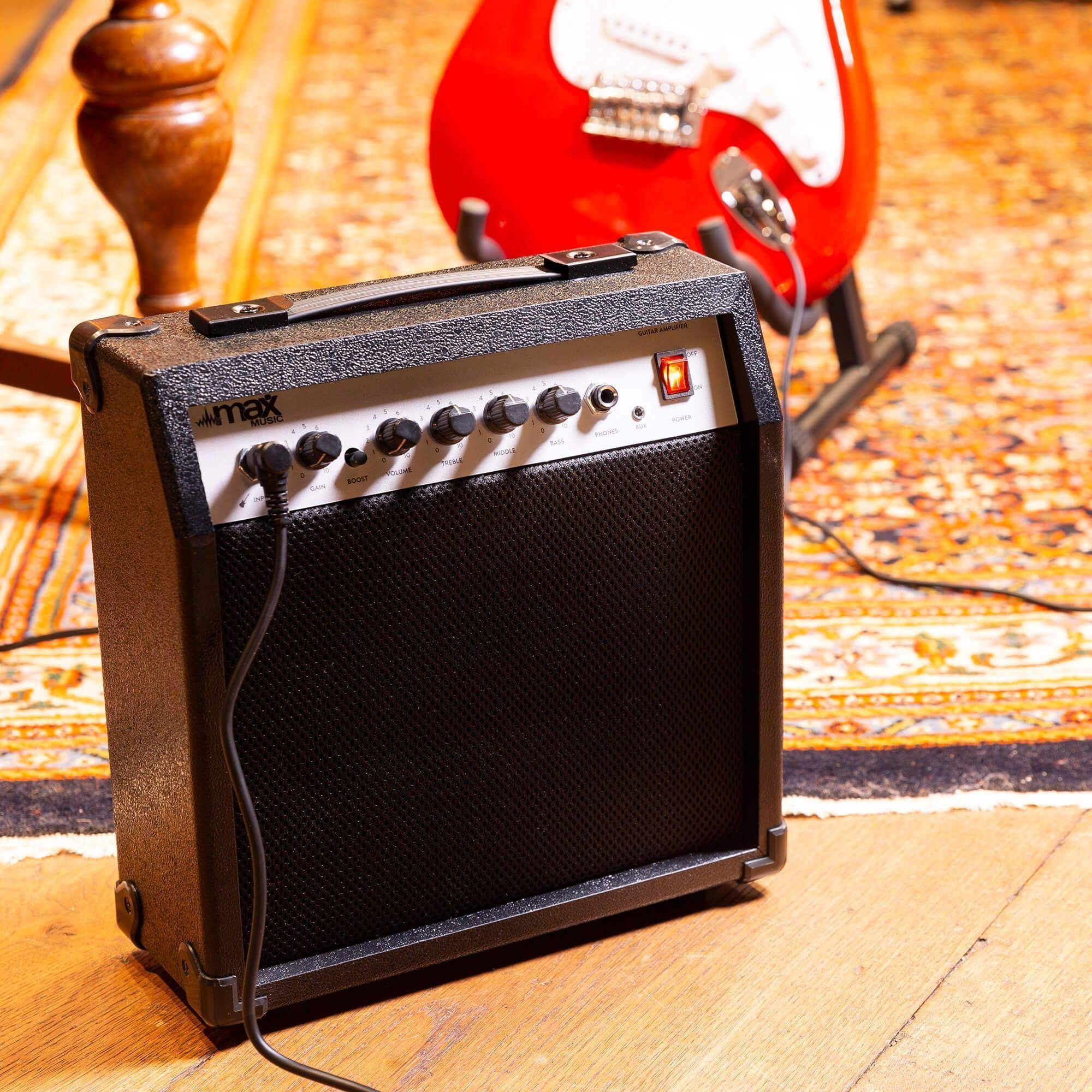 Amplificateur de guitare noir avec des boutons et un voyant d'alimentation. Une guitare rouge en arrière-plan.