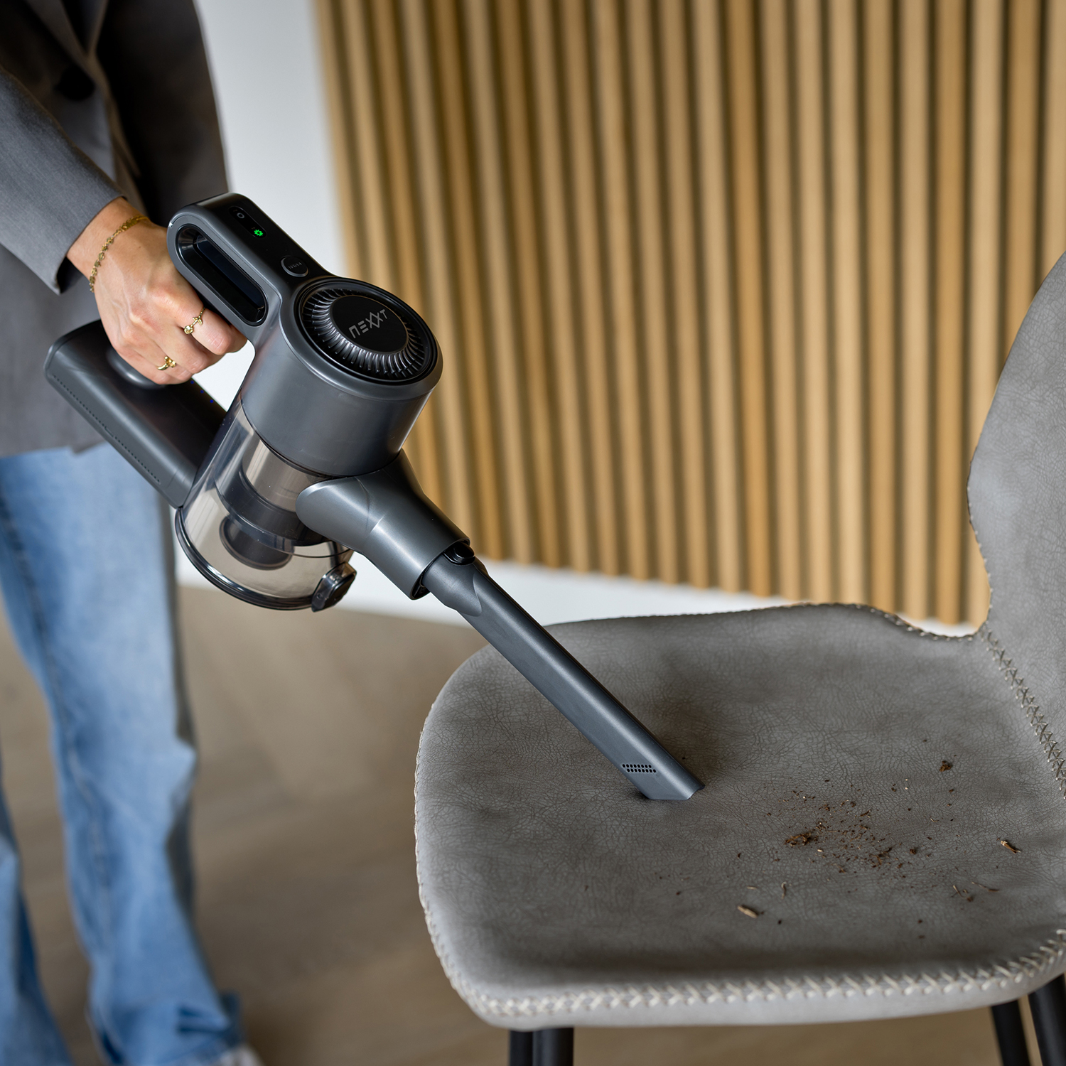 Person using a handheld vacuum cleaner to clean a gray chair. The chair has dirt on it.