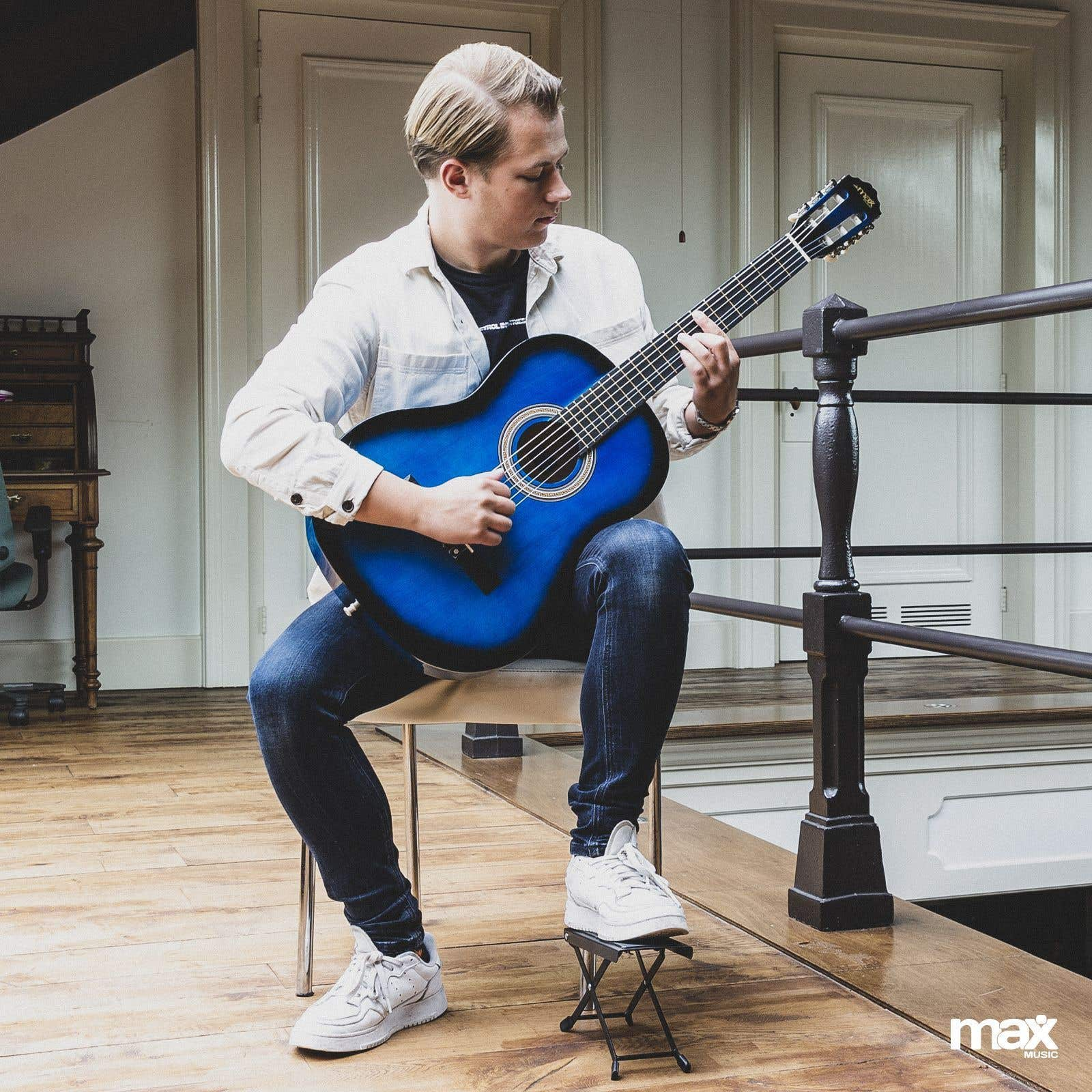 Junger Mann spielt eine blaue Akustikgitarre im Sitzen. Weißer Hintergrund.