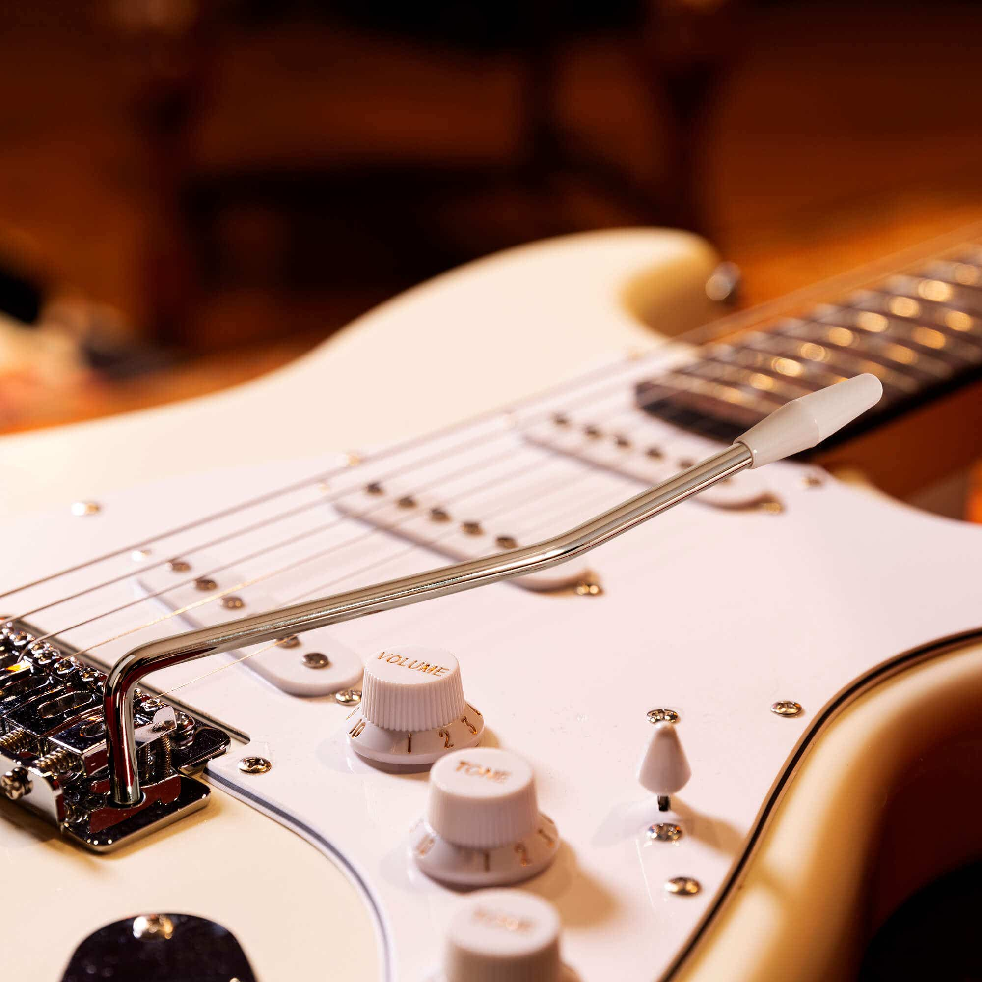 Nahaufnahme einer weißen E-Gitarre. Knöpfe und Steg sind sichtbar. Der Hintergrund ist unscharf.
