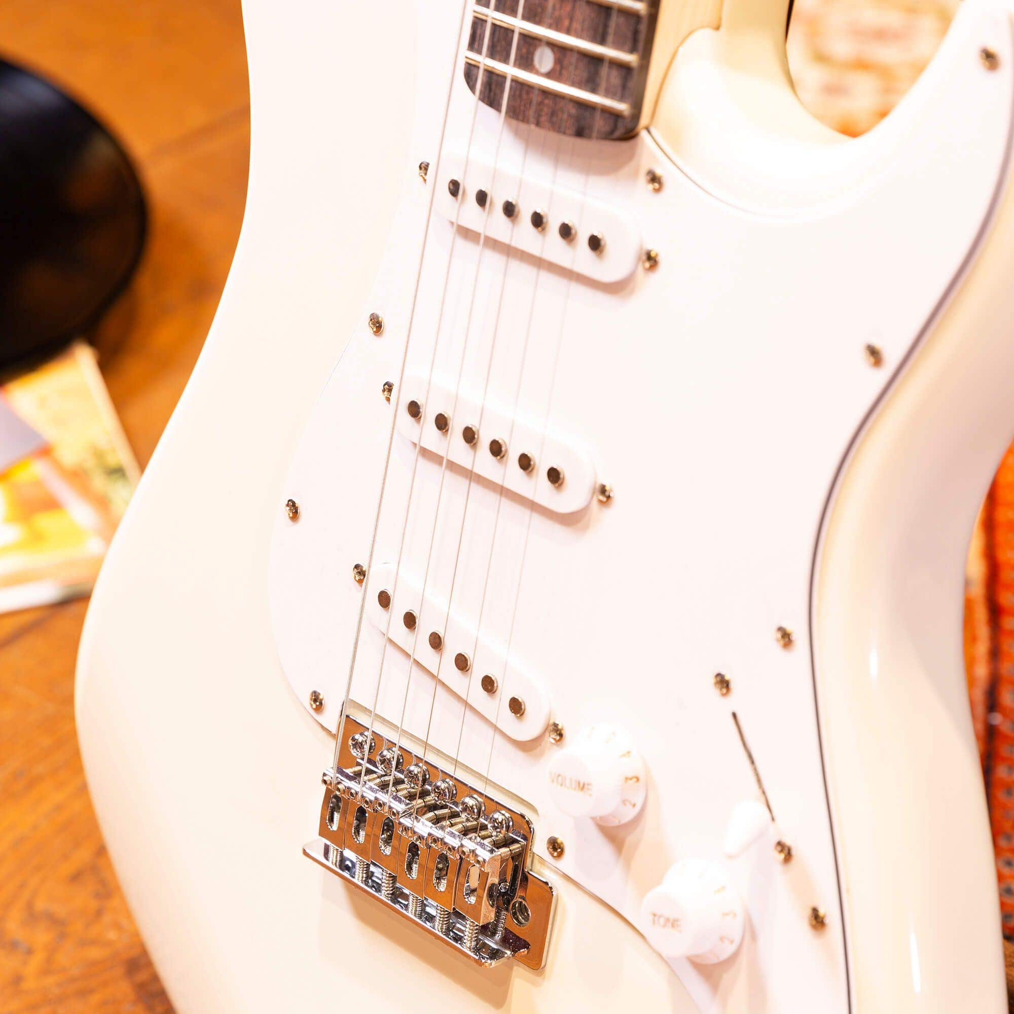 Nahaufnahme einer weißen E-Gitarre mit Knöpfen, Saiten und Chrom-Hardware.