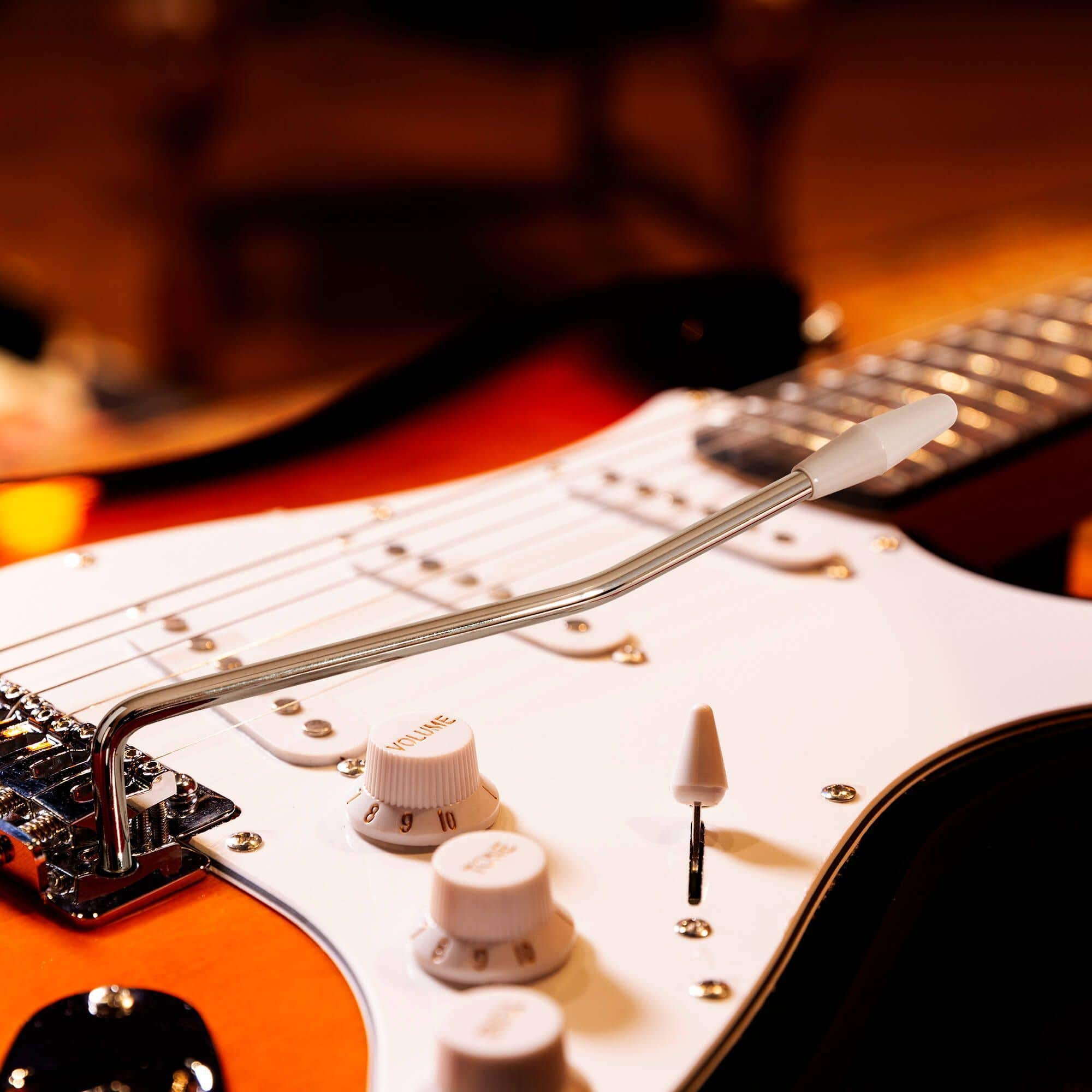 Nahaufnahme einer E-Gitarre mit weißem Schlagbrett, Knöpfen und Tremolohebel.