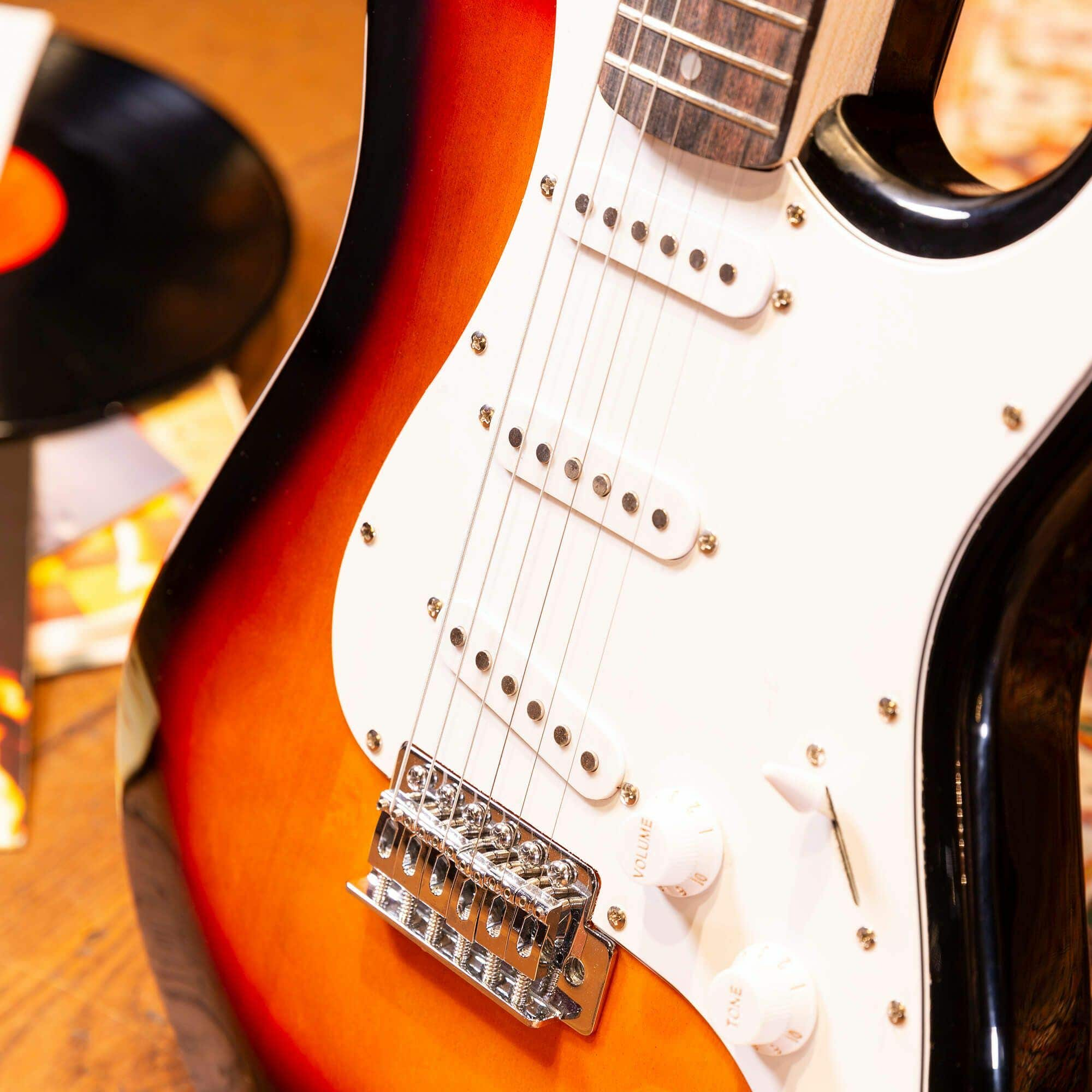 Gros plan sur une guitare électrique, dégradé orange-noir, plaque de protection blanche et boutons.