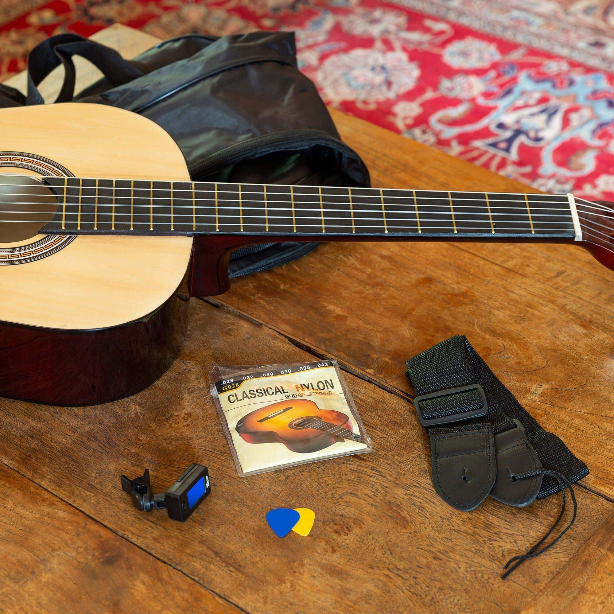 Eine Gitarre, ein Koffer, ein Stimmgerät, Plektren und ein Gurt auf einem Holztisch. Saiten sind ebenfalls sichtbar.