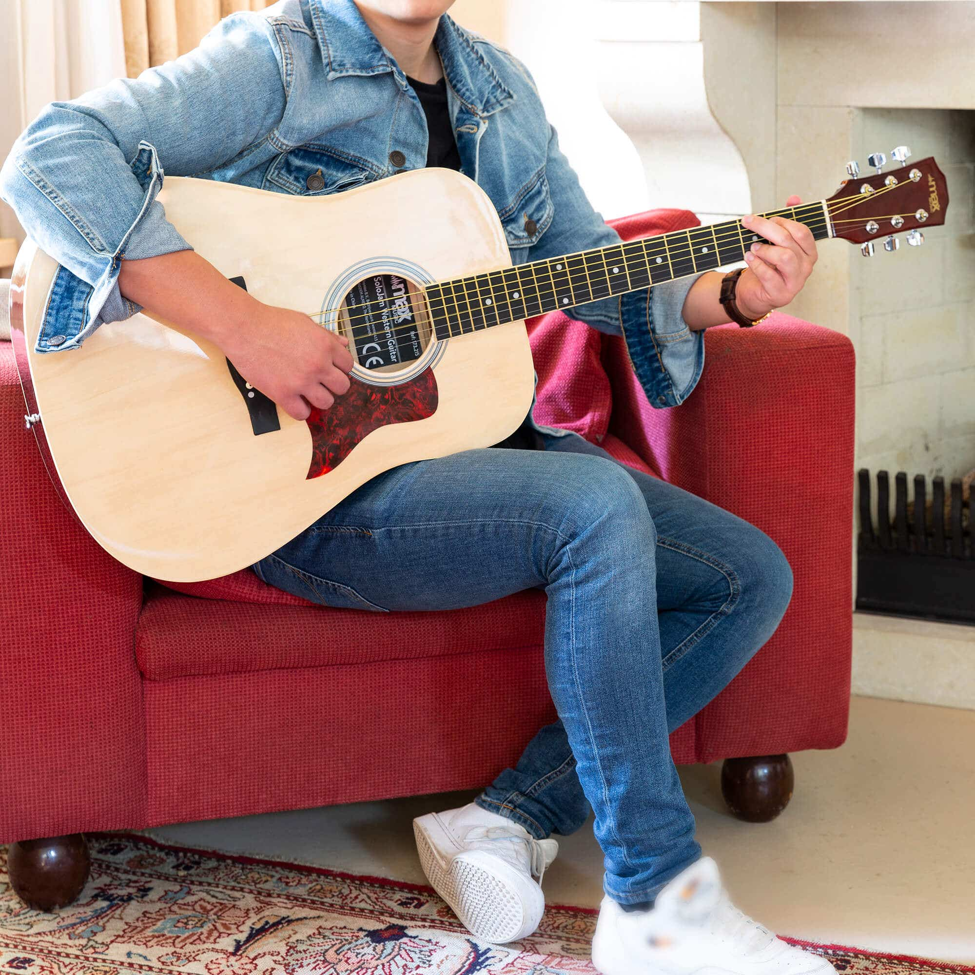 Een persoon zit op een rode bank en speelt akoestische gitaar.