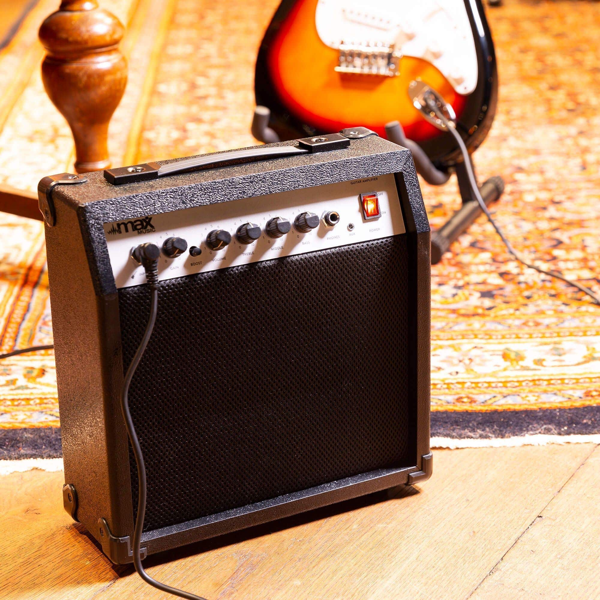 Un petit amplificateur de guitare noir sur un sol en bois avec une guitare en arrière-plan.