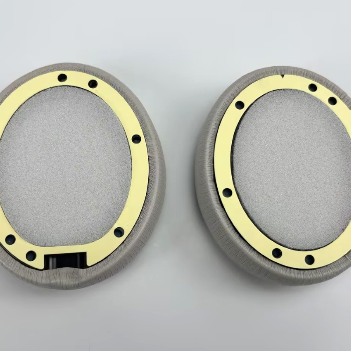 Dwie szare nausznice słuchawek ze złotymi obwódkami, okrągłe z centralnymi otworami.