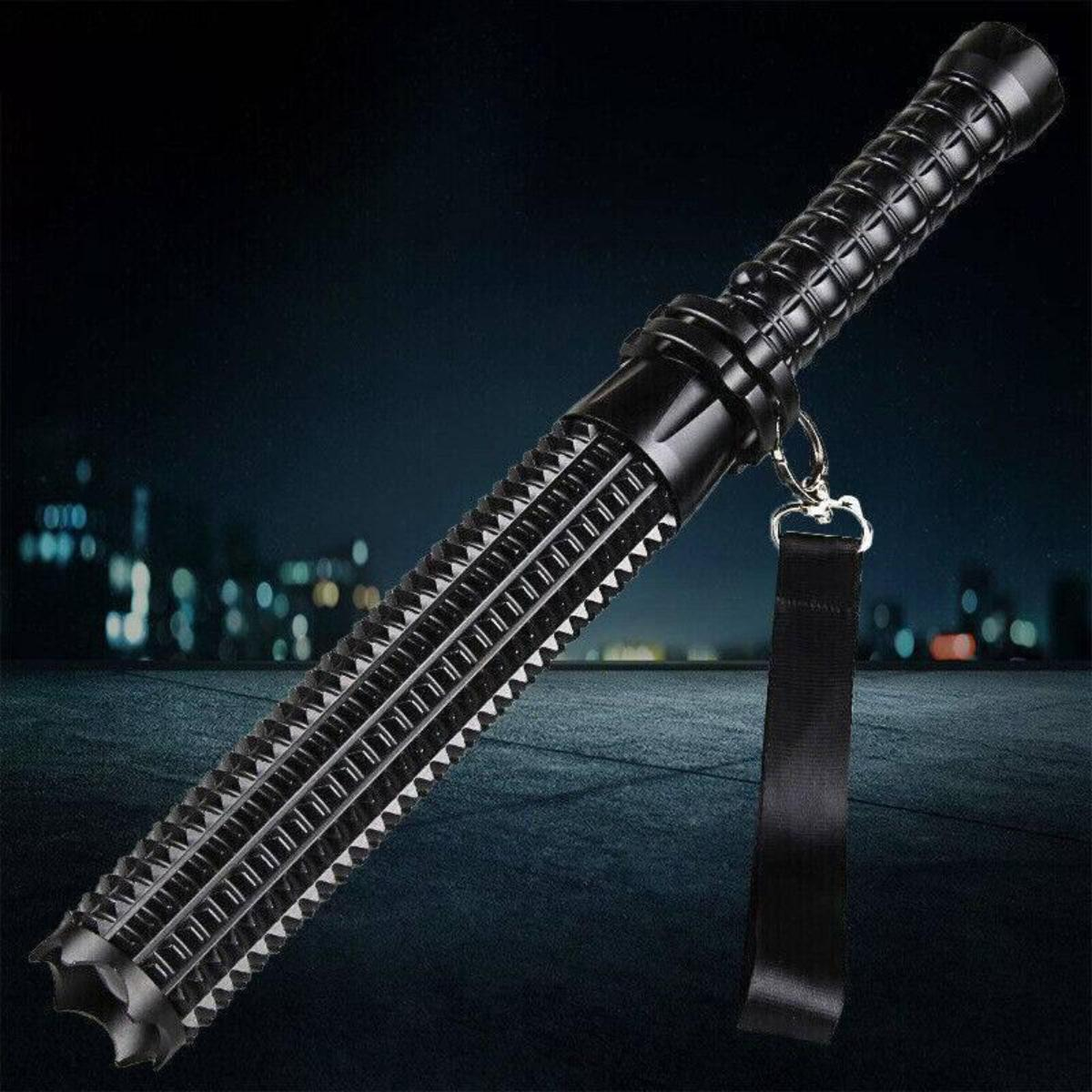 Eine schwarze, mehrteilige Taschenlampe mit Griff, Schlüsselband und schwarzem Riemen, vor unscharfem Hintergrund.