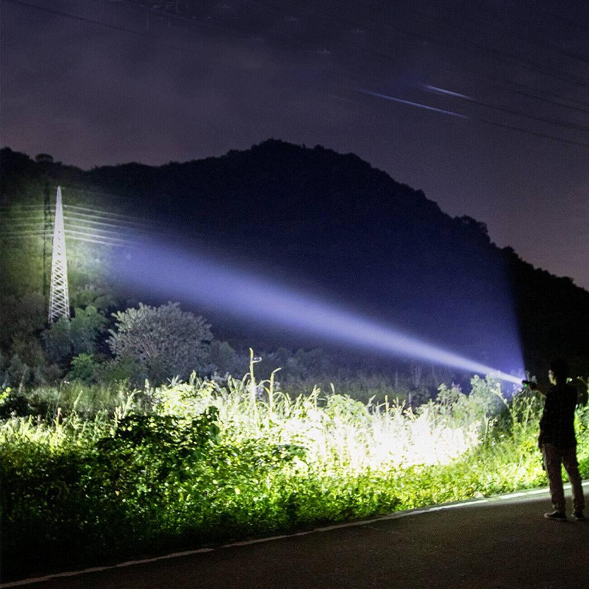 Eine Person leuchtet mit einer hellen Taschenlampe über ein Feld in der Nacht, mit einem entfernten Turm.