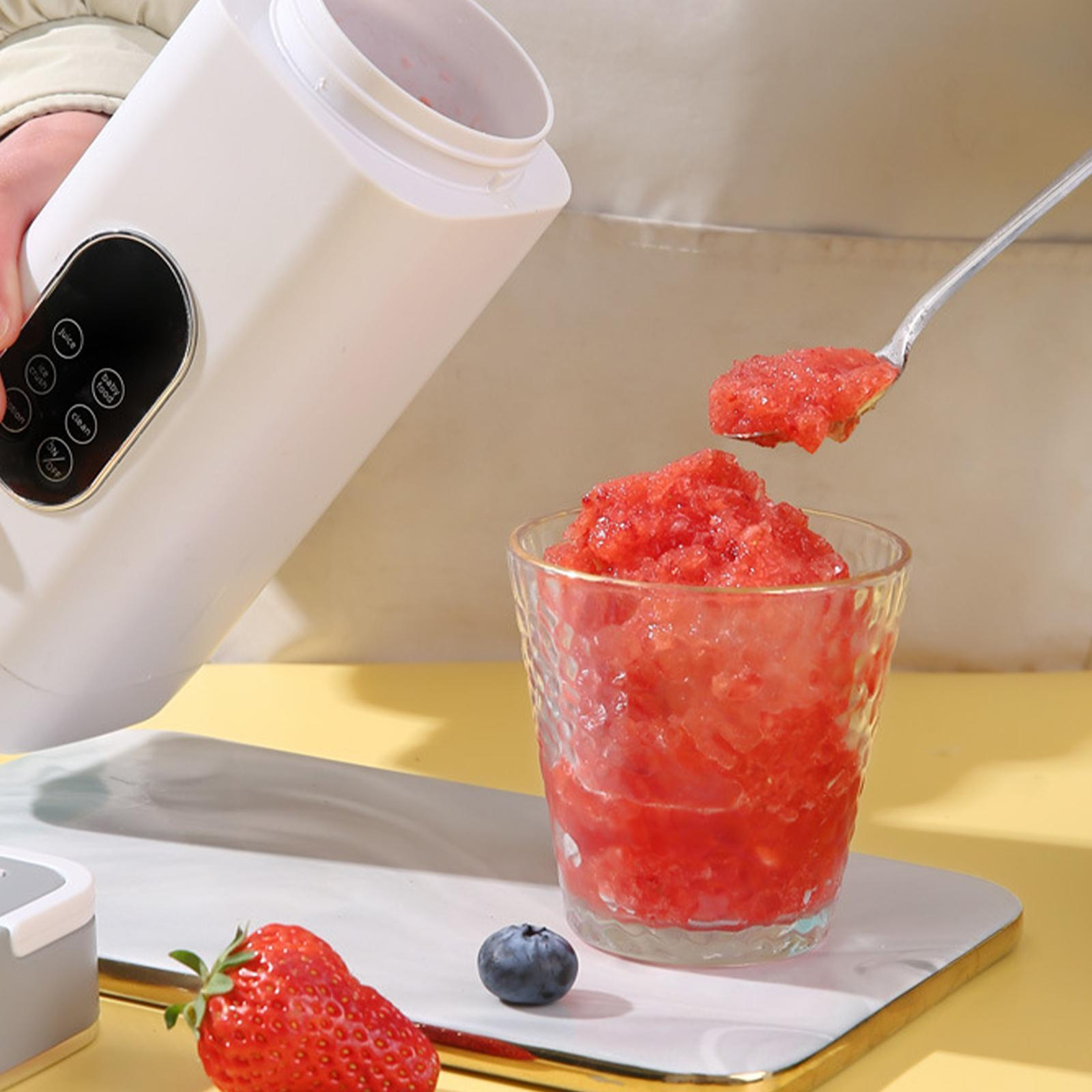 Ein Mixer gießt rosa Slush in ein Glas. Eine Erdbeere und eine Blaubeere liegen auf dem Tisch.