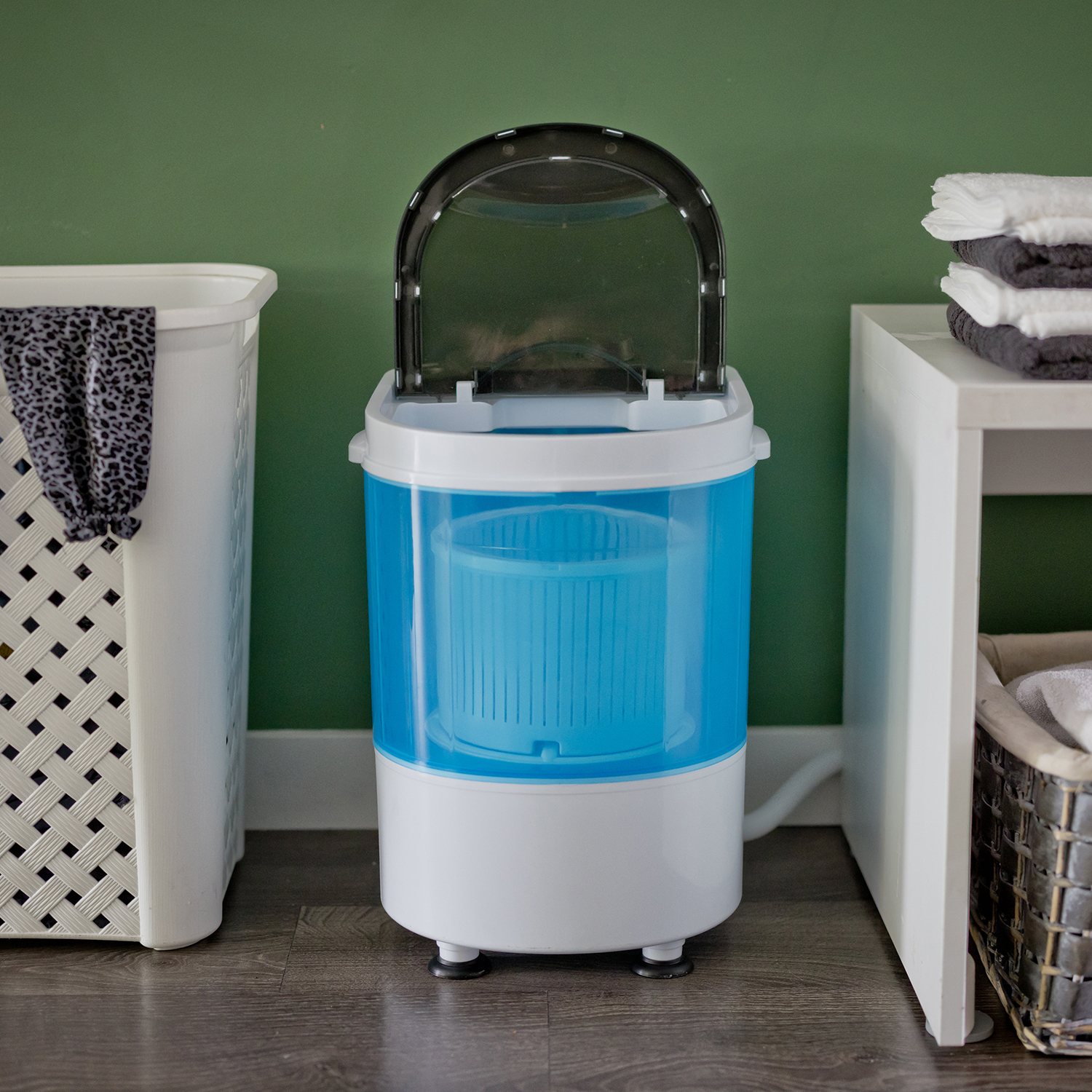 A blue and white portable washing machine with the lid open. A white basket and towels are in the background.