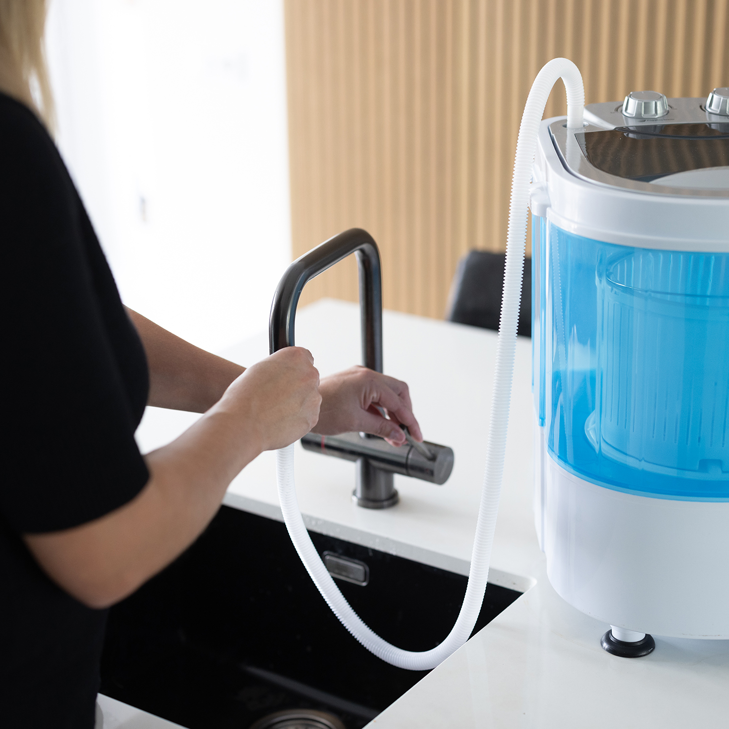 Woman near a small washing machine with a hose connected to a kitchen faucet.