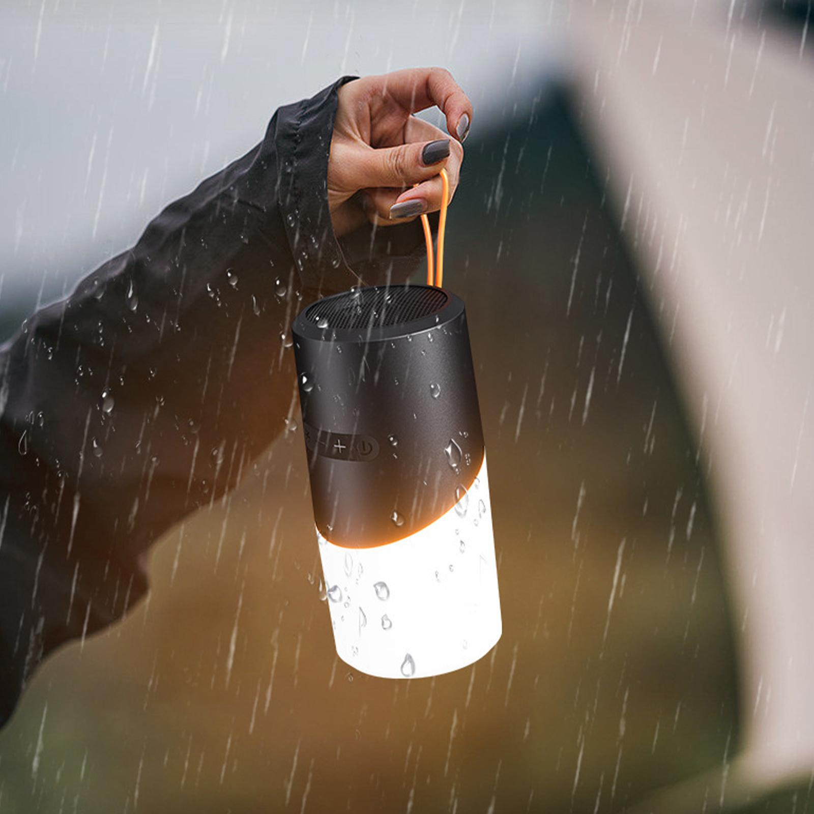 Eine Hand hält einen schwarz-weißen Lautsprecher im Regen. Regentropfen sind sichtbar. Oranger Riemen.