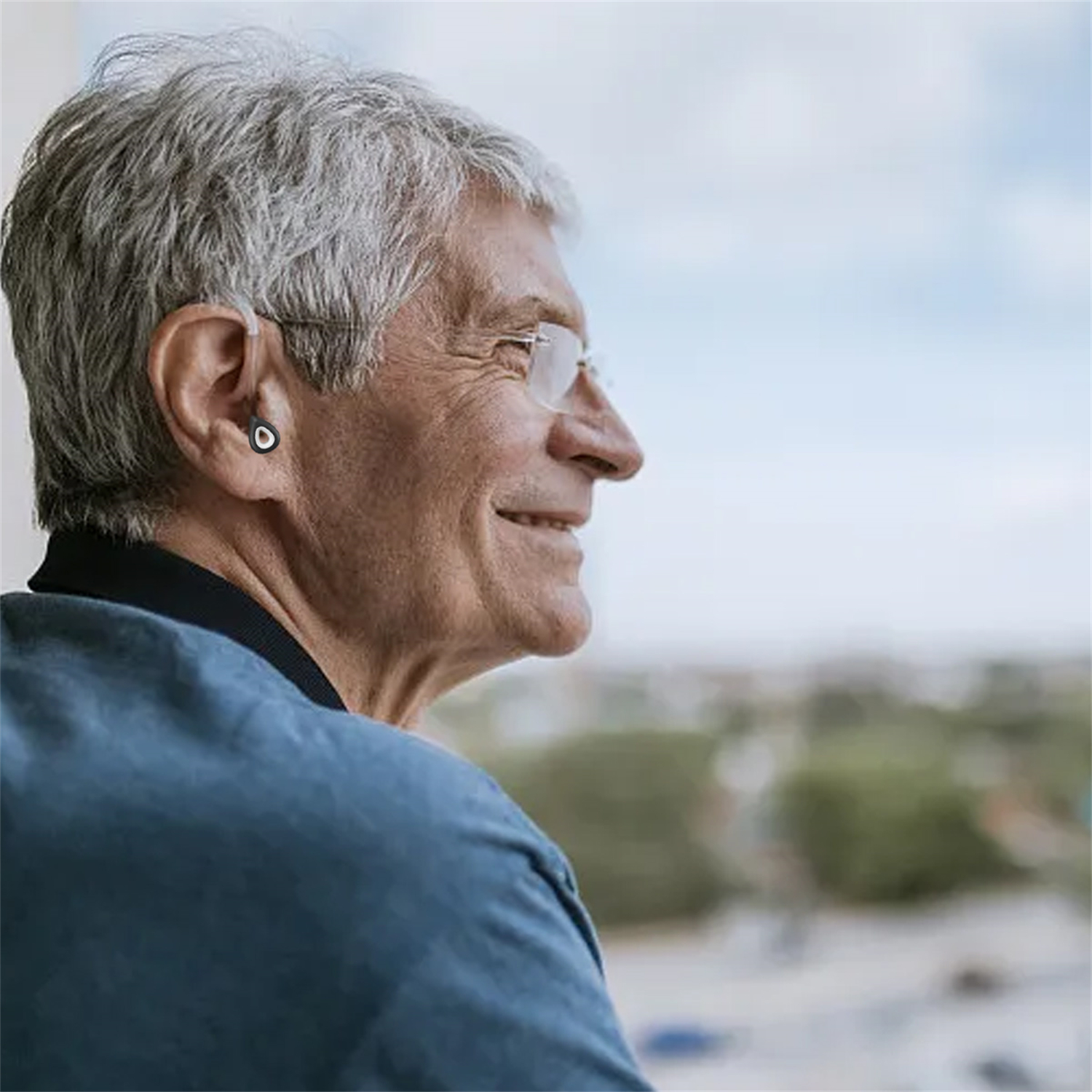 Älterer Mann mit Brille und Hörgerät, blickt aus dem Fenster.