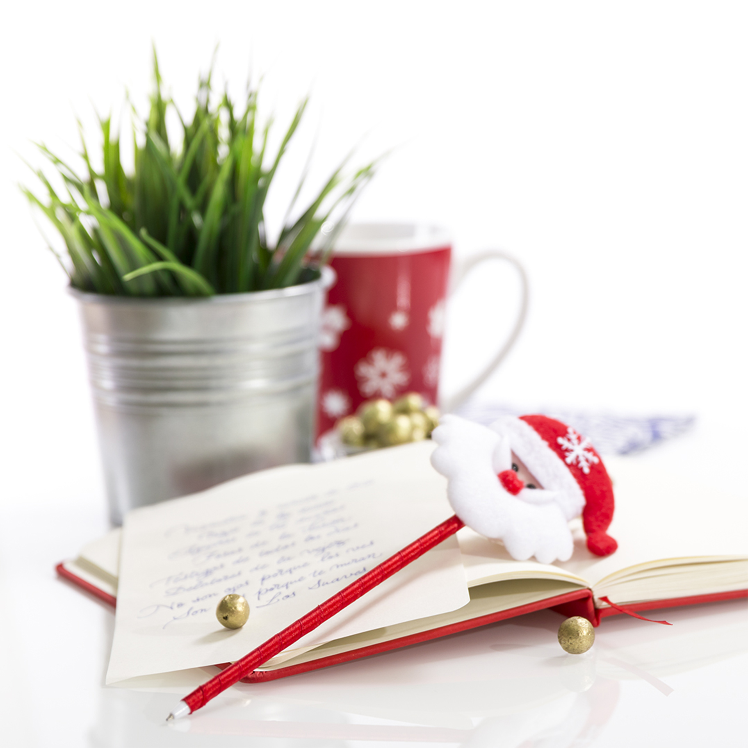Eine Weihnachtsszene mit Notizbuch, Stift, Weihnachtsmützenstift und goldenen Ornamenten. Ein Becher und ein Blumentopf sind im Hintergrund.
