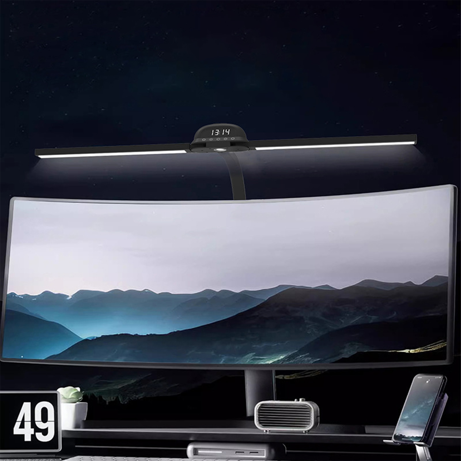 Schwarze Schreibtischlampe über einem gebogenen Monitor, der eine Berglandschaft zeigt. Die Uhr zeigt 13:14 Uhr. Auf dem Schreibtisch befinden sich Telefon, Uhr, Lautsprecher und eine kleine Pflanze.