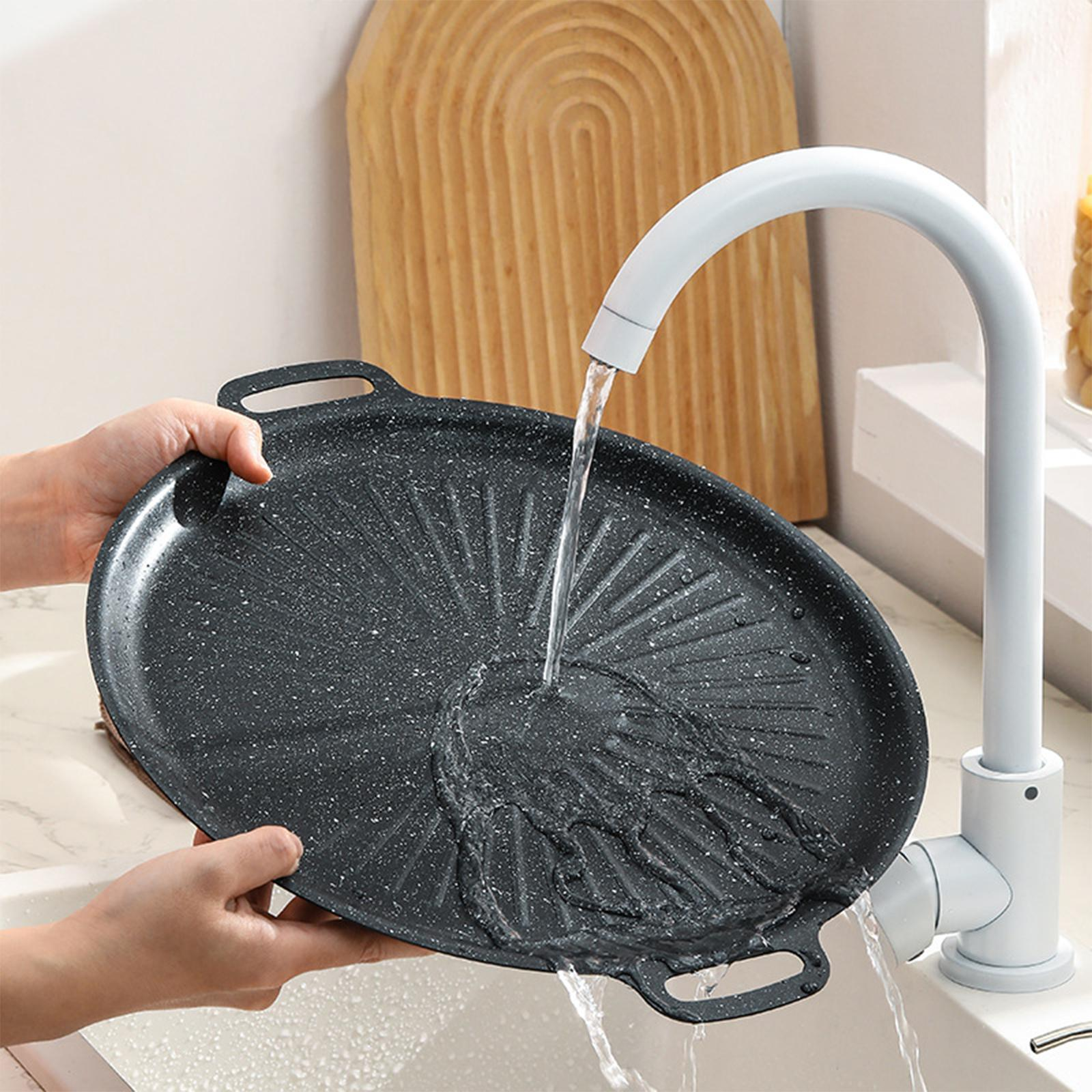 Schwarze Antihaftpfanne wird mit Wasser aus einem weißen Wasserhahn gespült.