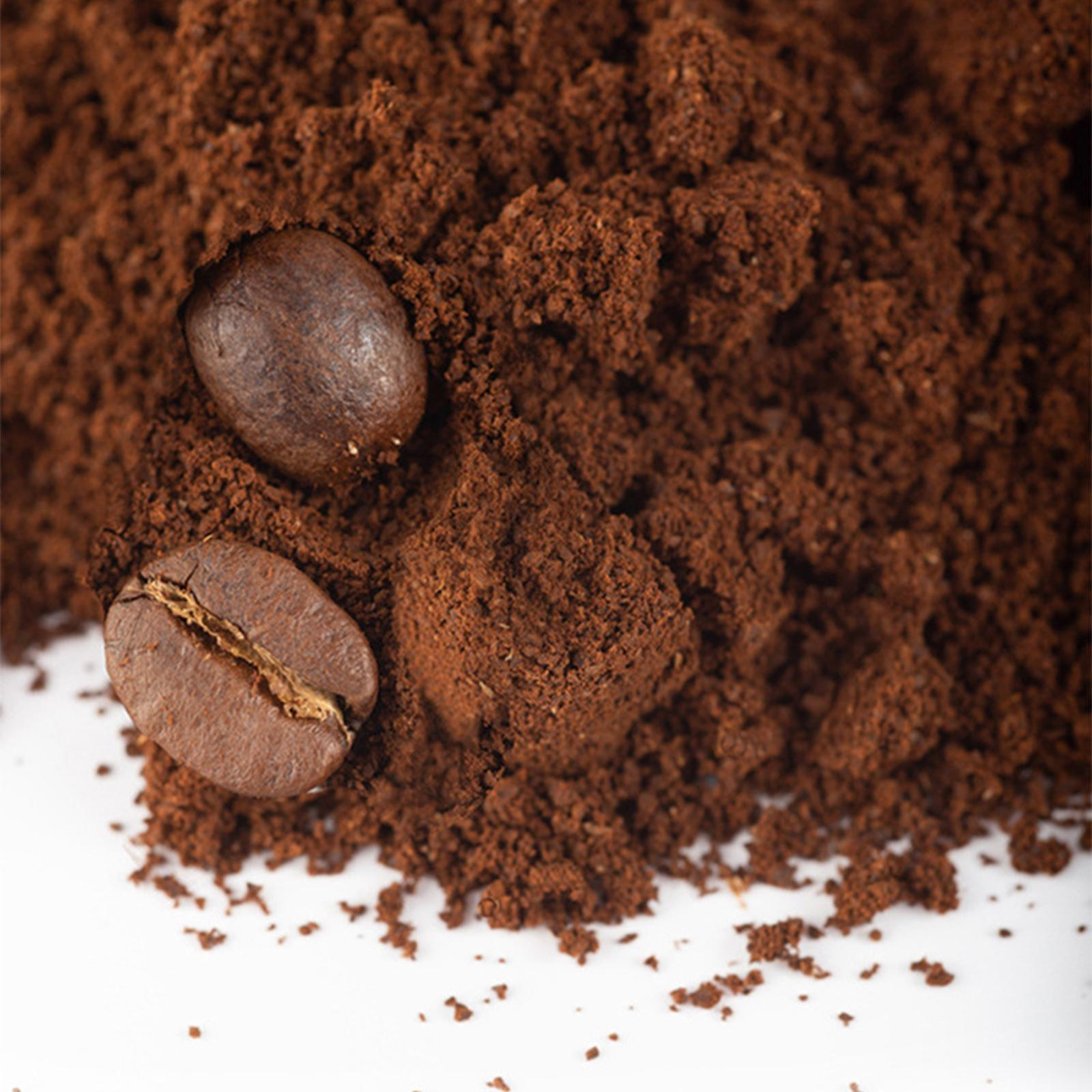 Nahaufnahme von Kaffeepulver und zwei Kaffeebohnen. Brauntöne, weißer Hintergrund. Fokus auf Textur und Detail.