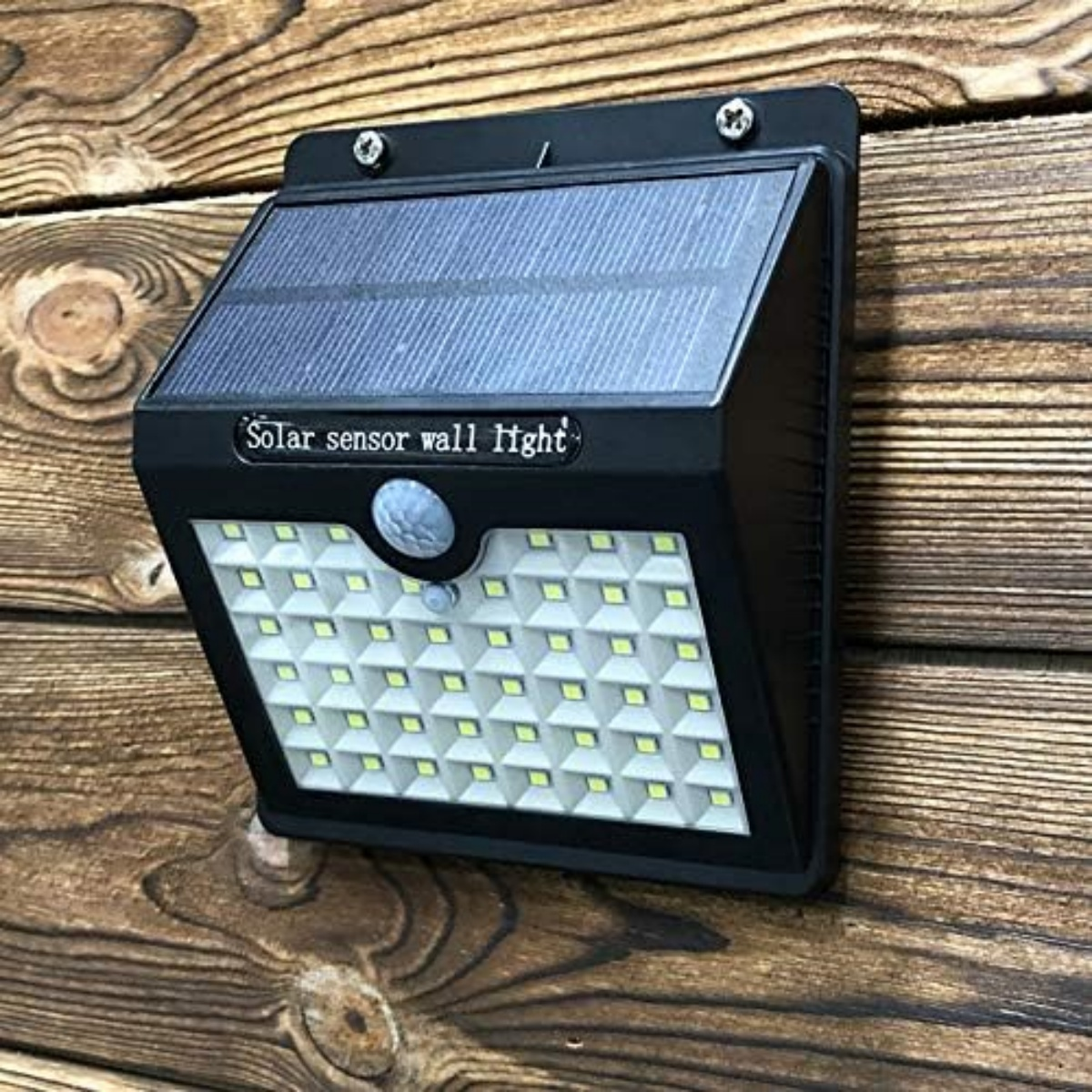 Eine schwarze Solar-Sensor-Wandleuchte, die an einer Holzwand montiert ist.