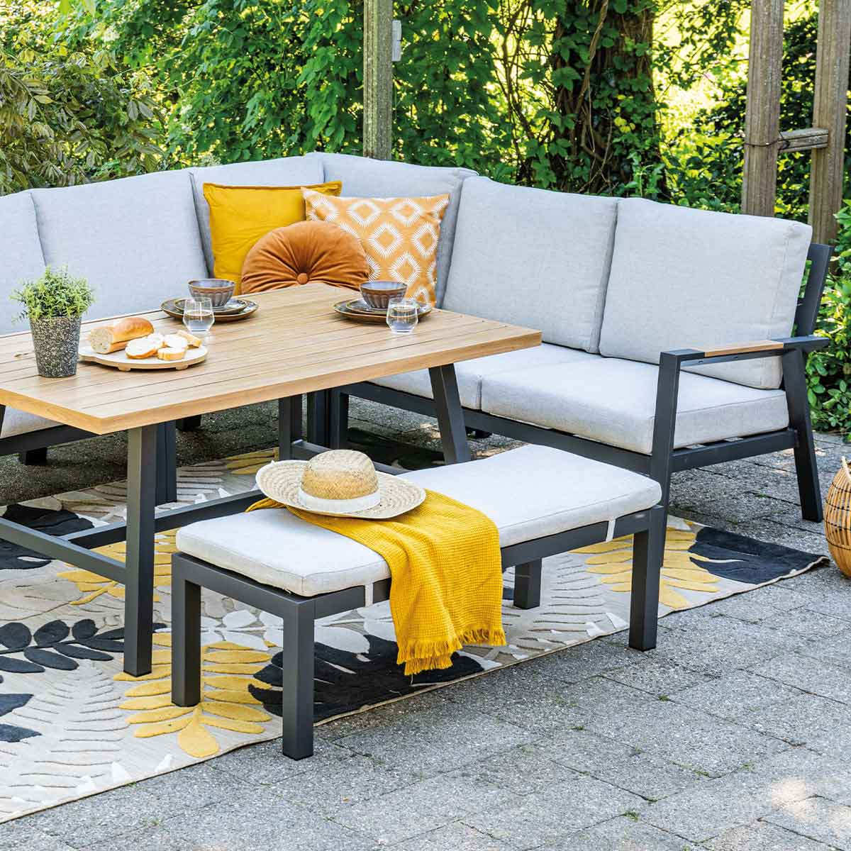 Outdoor seating area with a table, bench, and corner sofa. Rug and pillows are also present.