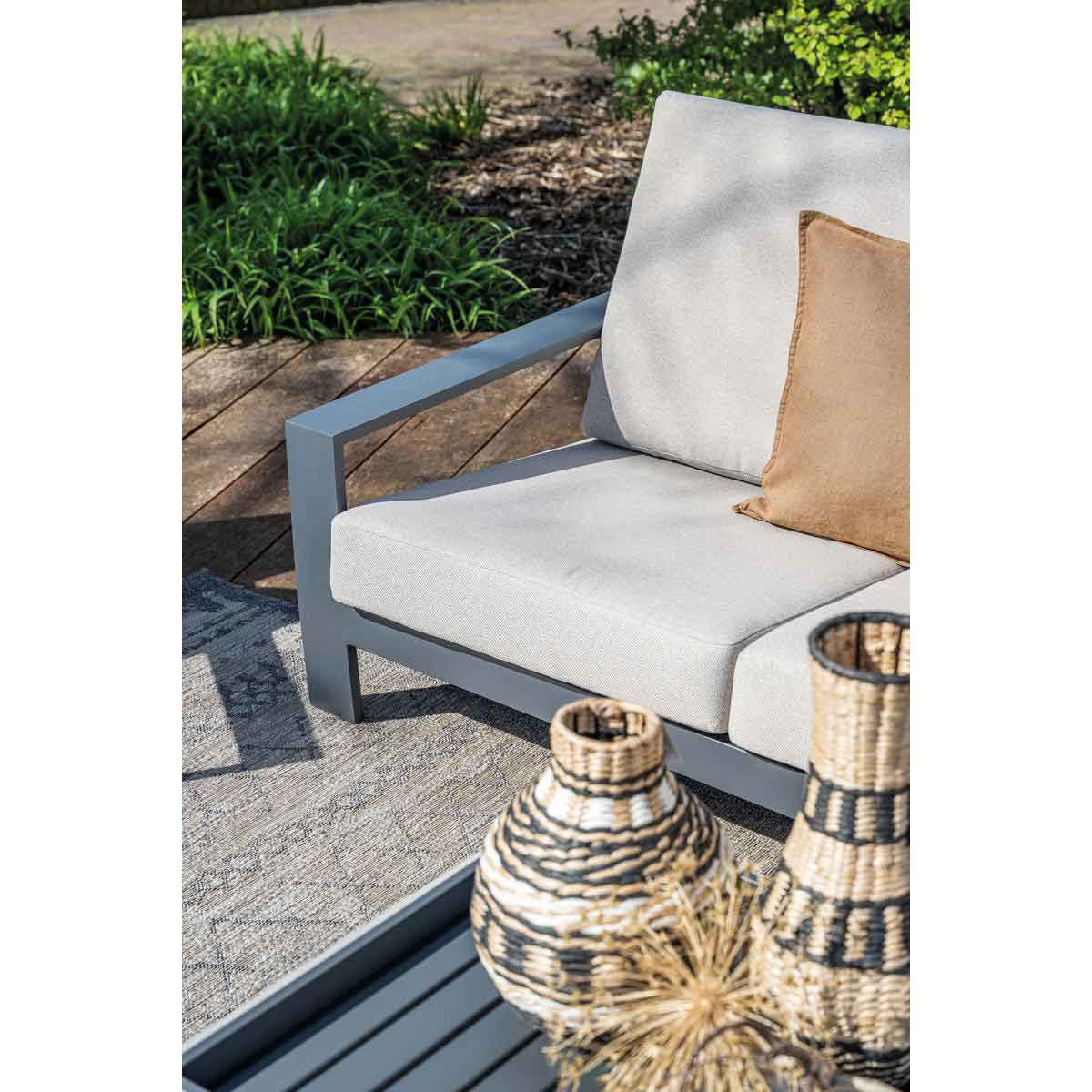 Modern outdoor seating with gray cushions, brown pillow, and decorative vases on the table.