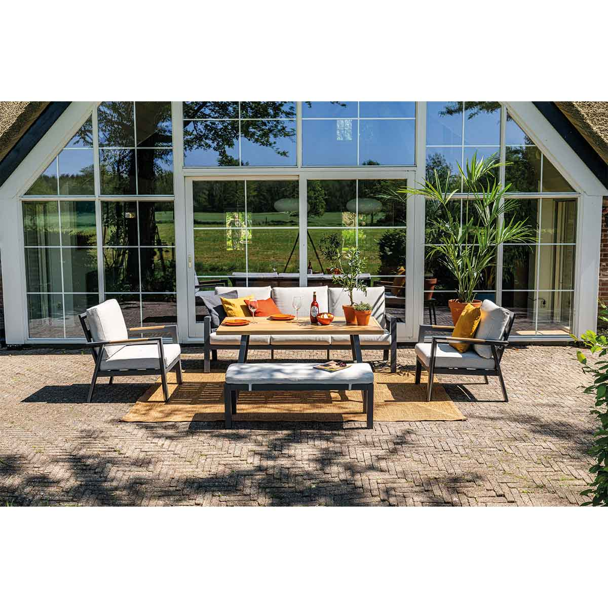 Zithoek in de openlucht met een bank, twee fauteuils, een bank en een tafel voor een huis.
