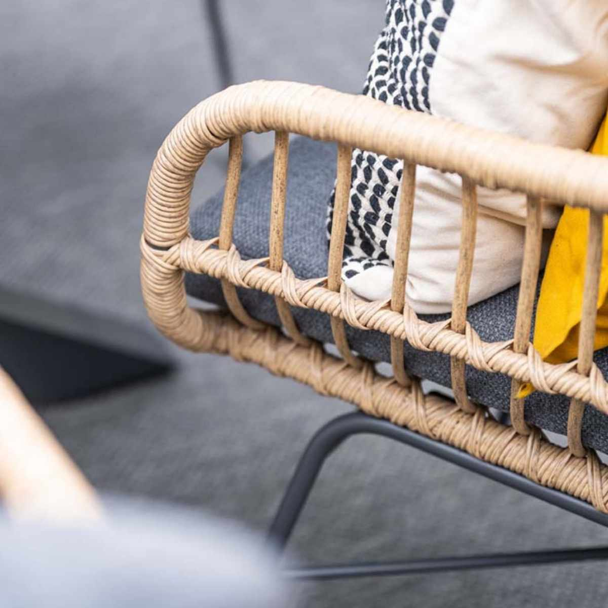 Rotan stoel detail: armleuning, grijs kussen, gele kussen. Geweven textuur.