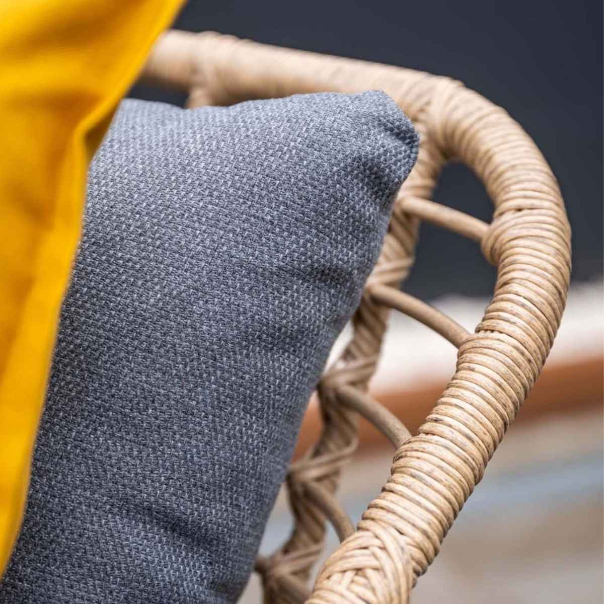Close-up van een geweven stoeldetail met een grijs kussen en een gele kussen.