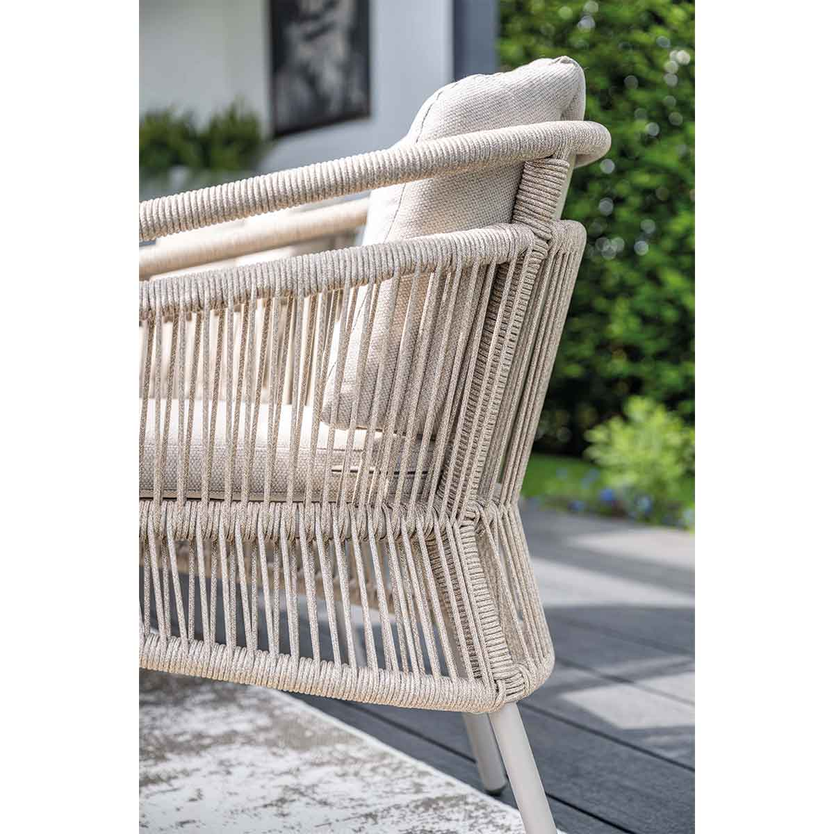Rattan chair detail: woven back, beige cushion. Light wood deck.