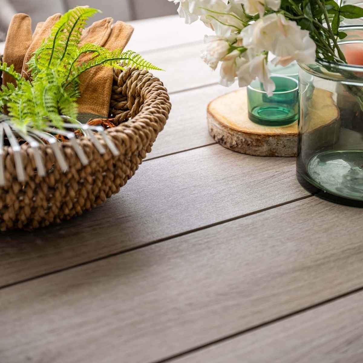 Een tafelsetting met een mand met planten, handschoenen, bloemen en een glazen pot.