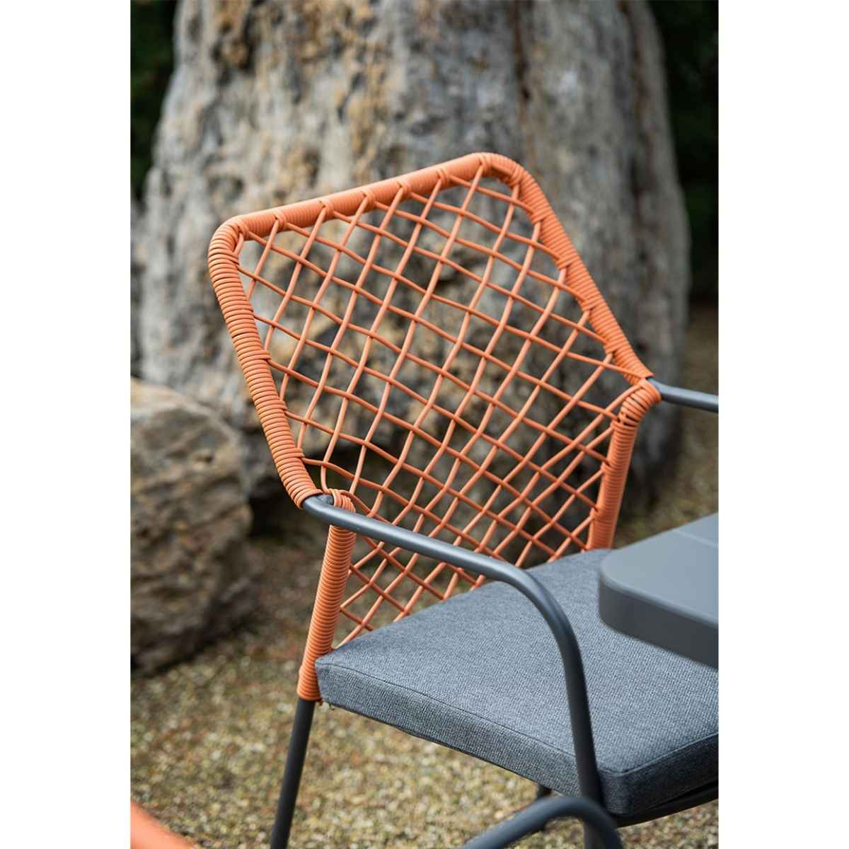 Close-up of chair. Orange rope design, gray cushion, and gray frame. Rock in the background.