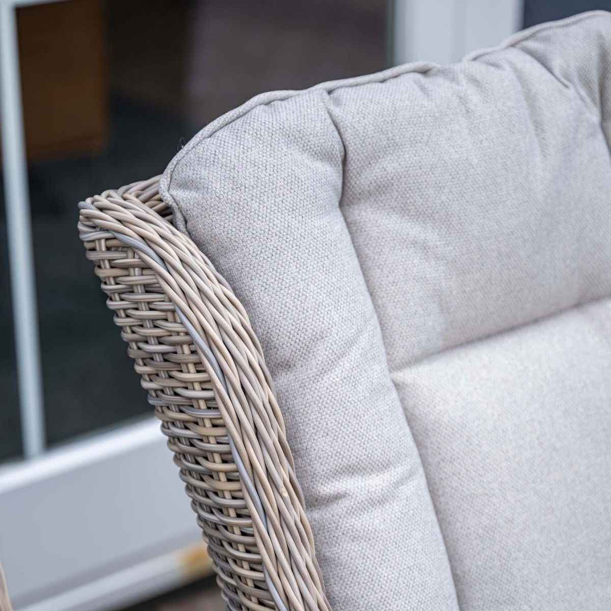 Close-up of a woven chair with a light-colored cushion. The chair has a natural weave pattern.