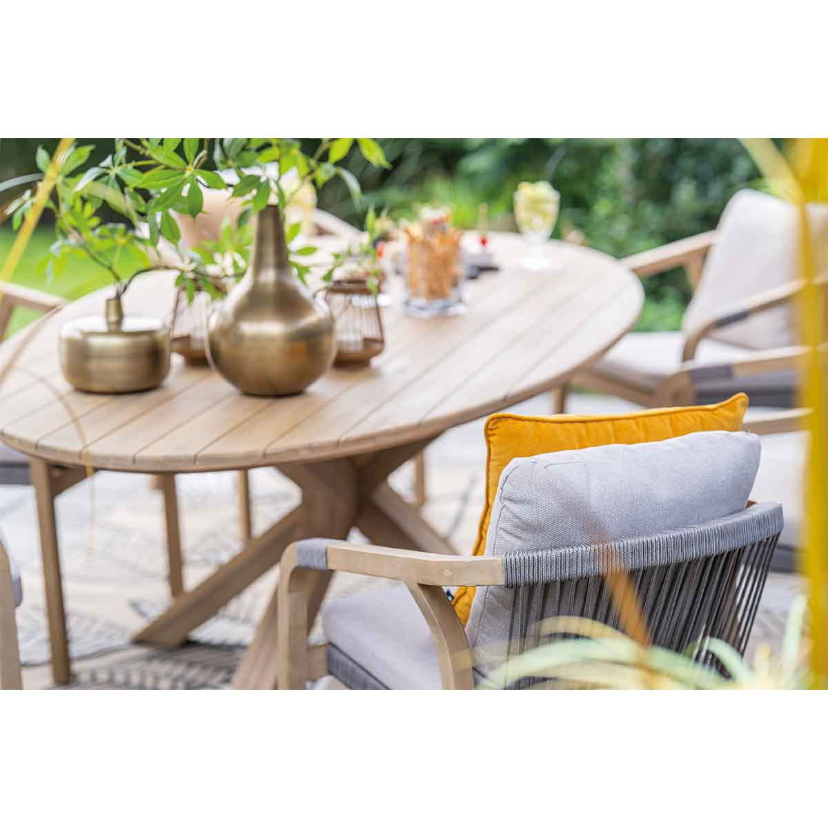 Ovale tafel met stoelen. Gouden vazen en geel kussen. Buitenomgeving.