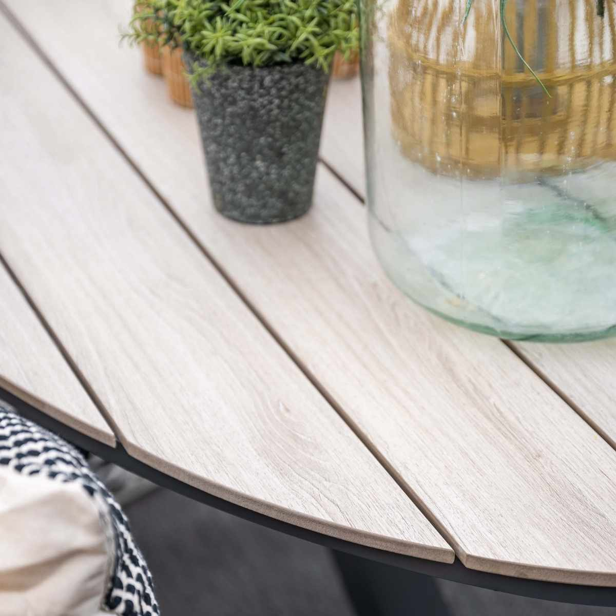 Close-up van een lichte houten tafel. Een potplant en een glazen pot staan op de tafel.