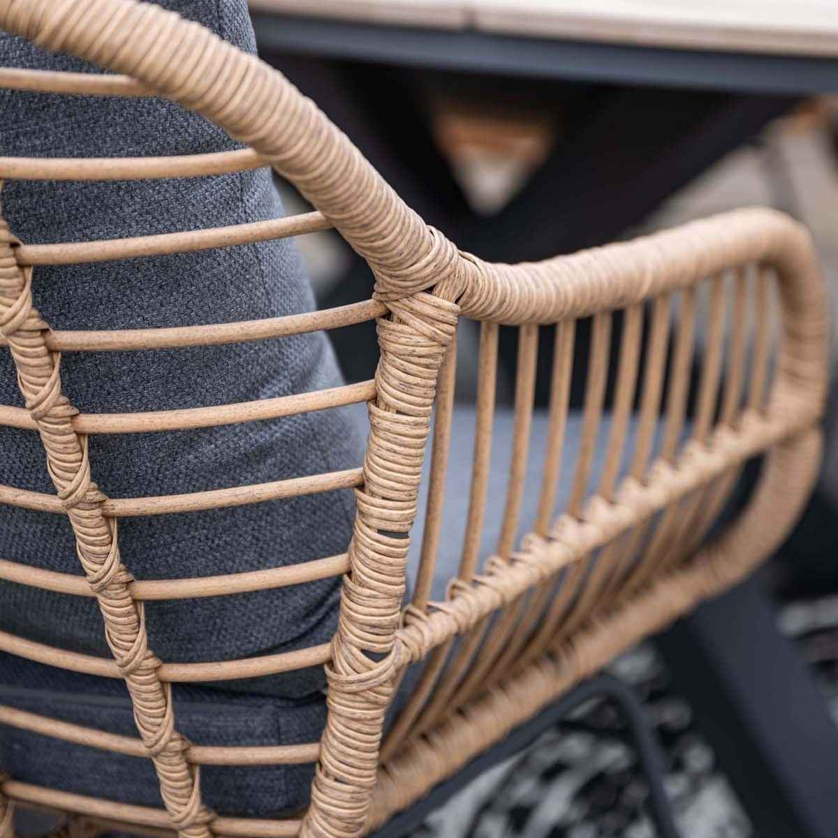Close-up van een stoel met rotan frame en grijs kussen.