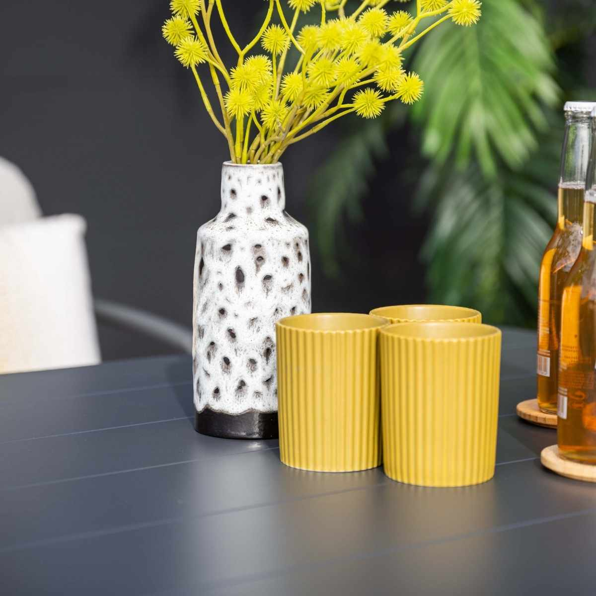 Yellow cups, flowers, and bottles on a gray table.